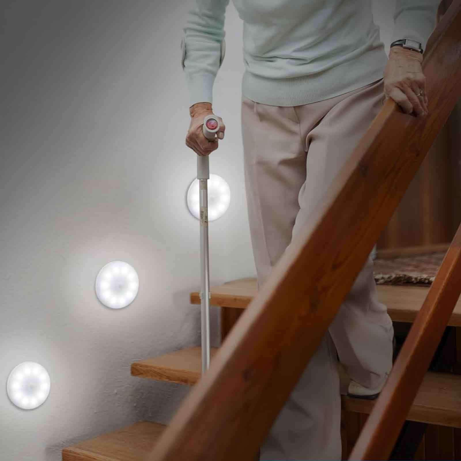 Eine Person mit einem Stock geht eine Treppe hinauf, beleuchtet von runden, weißen LED-Leuchten an der Wand.