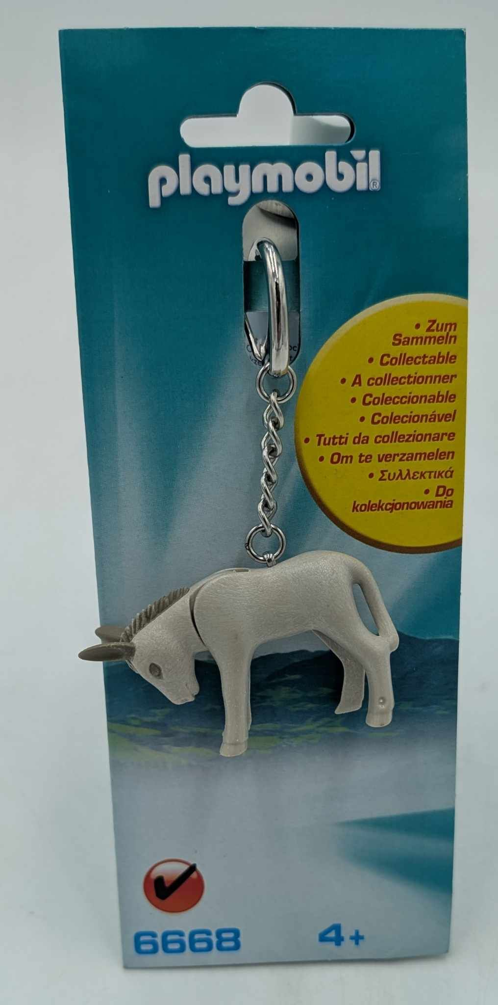 Un portachiavi Playmobil con una figura di asino bianco appesa a una carta blu e bianca.