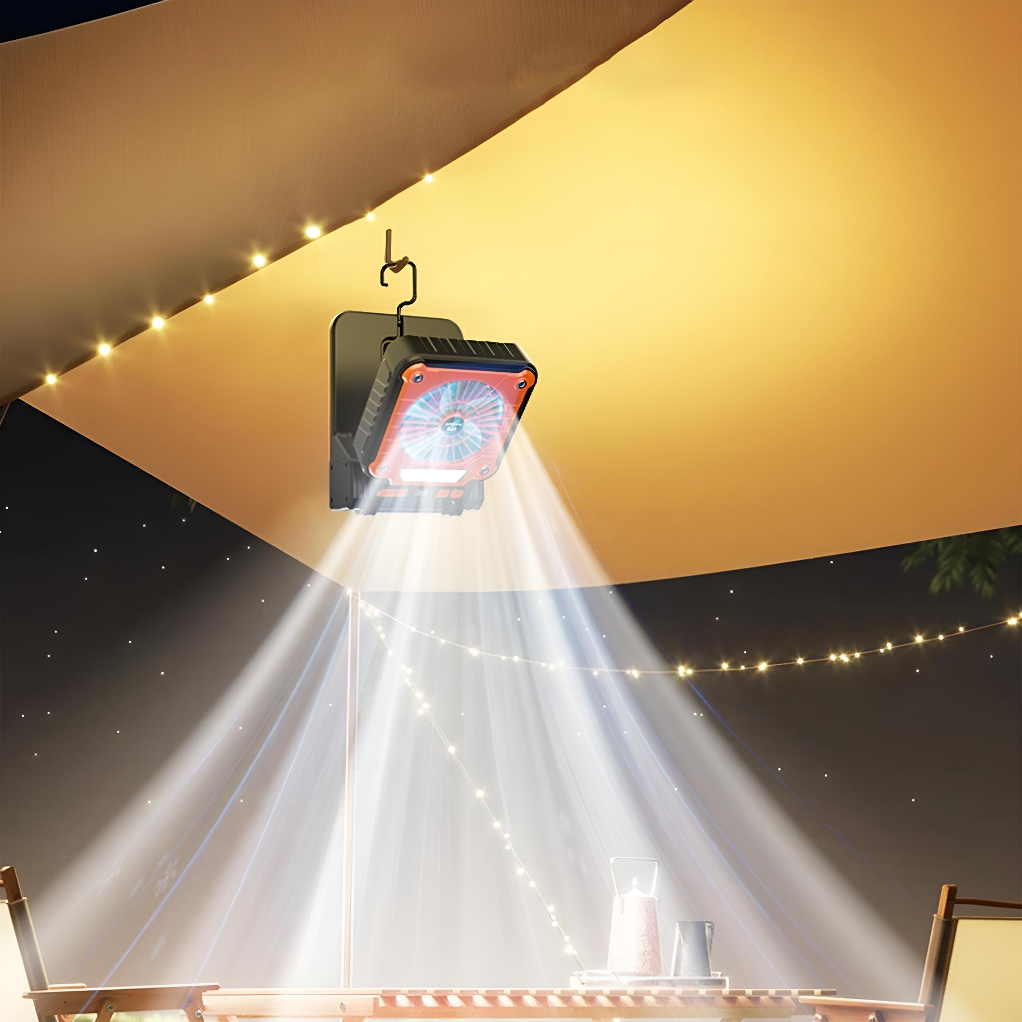 Eine Lüfterlampe, die unter einer braunen Plane hängt, mit einer Nachtszene. Lichter scheinen nach unten und ein Tisch darunter.
