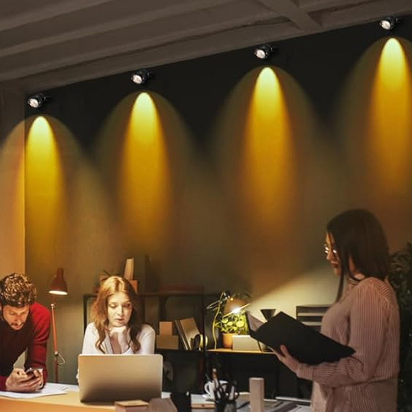 Büro mit Personen, die unter Scheinwerfern arbeiten und eine fokussierte und beleuchtete Umgebung schaffen.