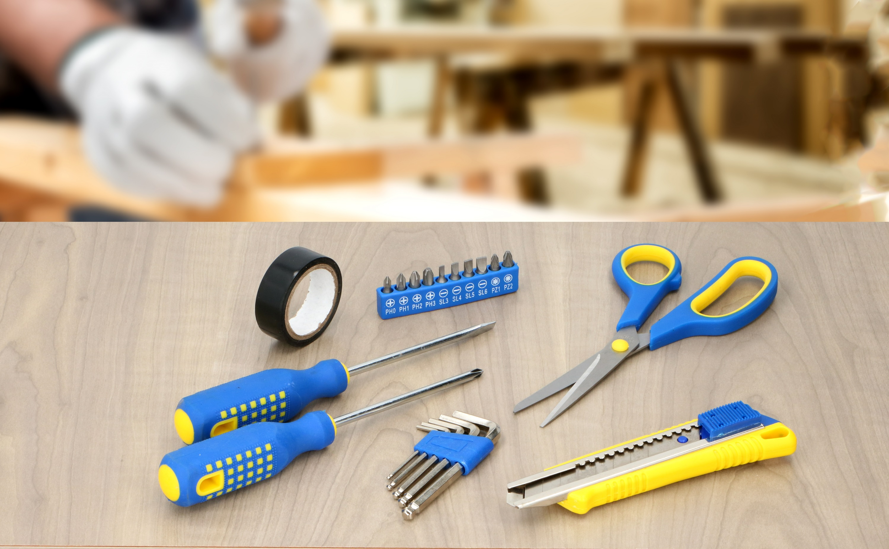 Outils : ruban adhésif, tournevis, embouts, ciseaux, cutter sur table en bois. Arrière-plan flou.