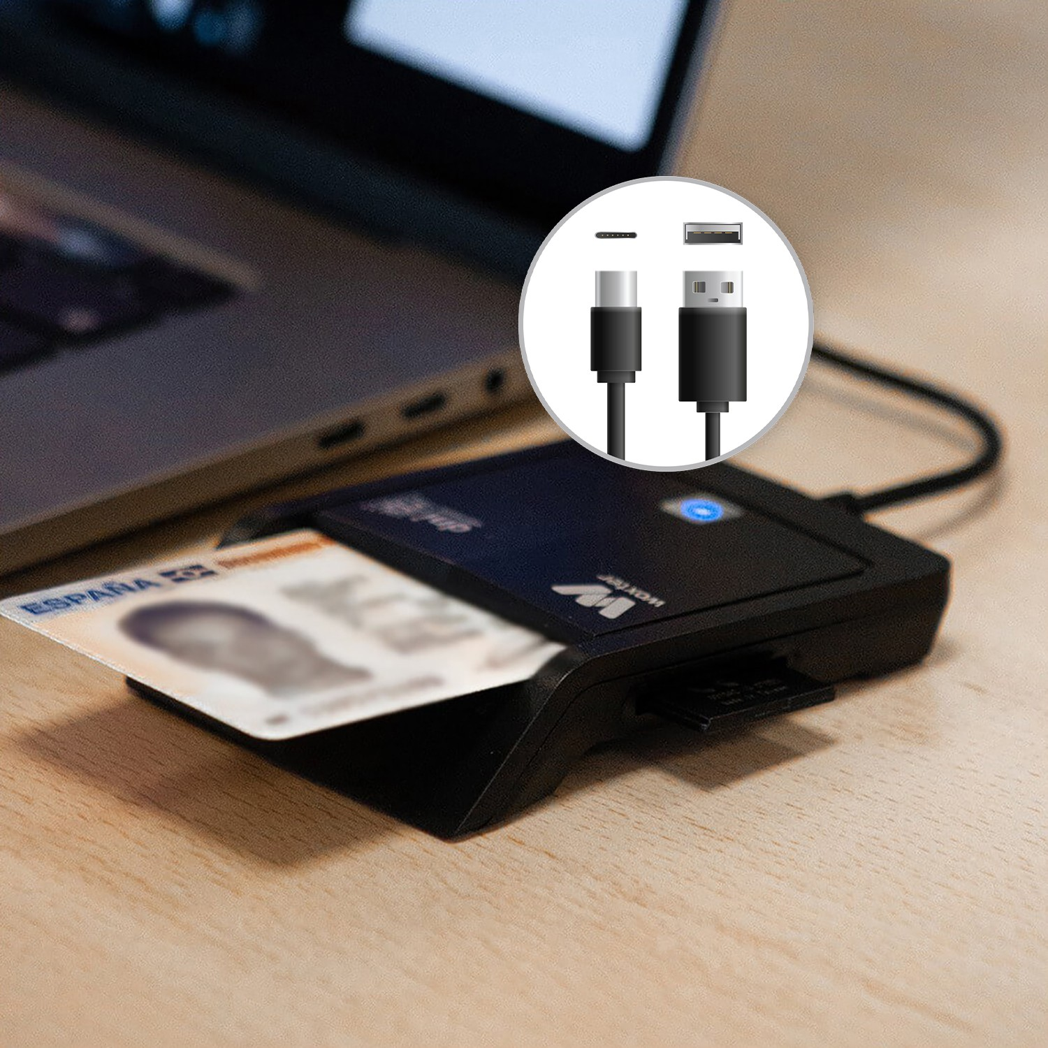Un lector de tarjetas negro con una tarjeta de identificación española insertada, cables USB y USB-C visibles. Un portátil al fondo.