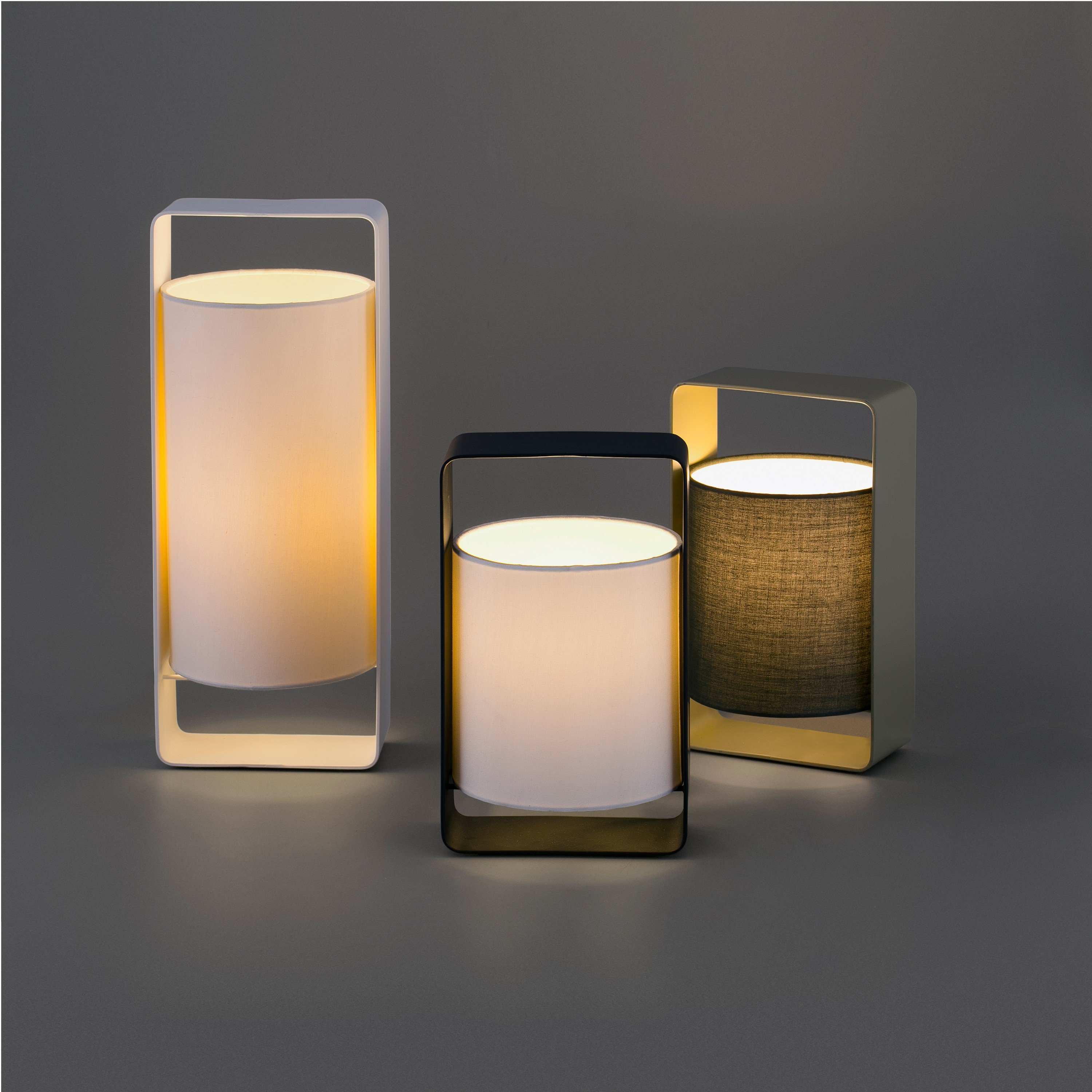 Tre lampade illuminate con paralumi in tessuto. Cornici bianche, nere e dorate su sfondo grigio. La luce brilla.
