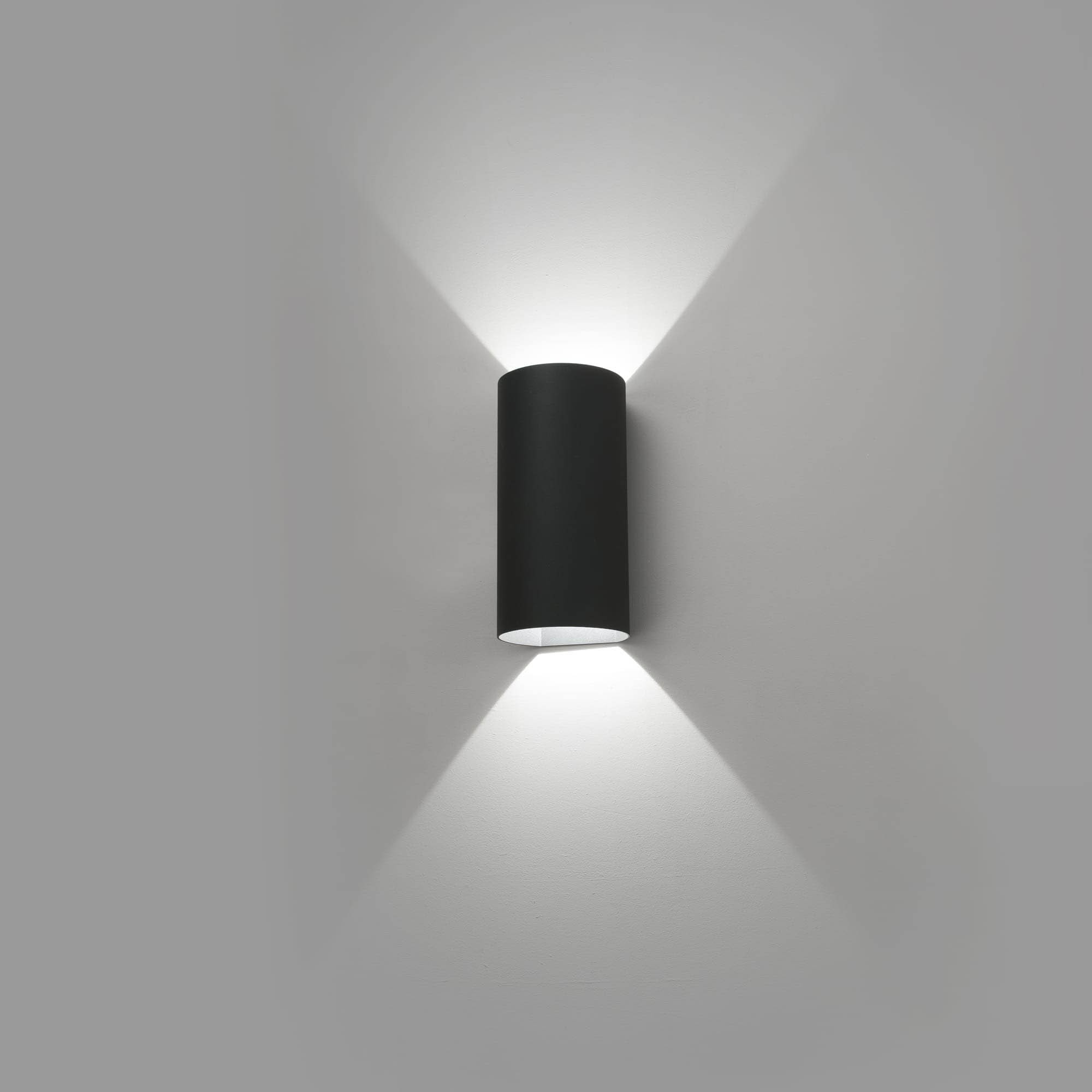 Schwarze zylindrische Außenlampe an weißer Wand, die Licht nach oben und unten abstrahlt.