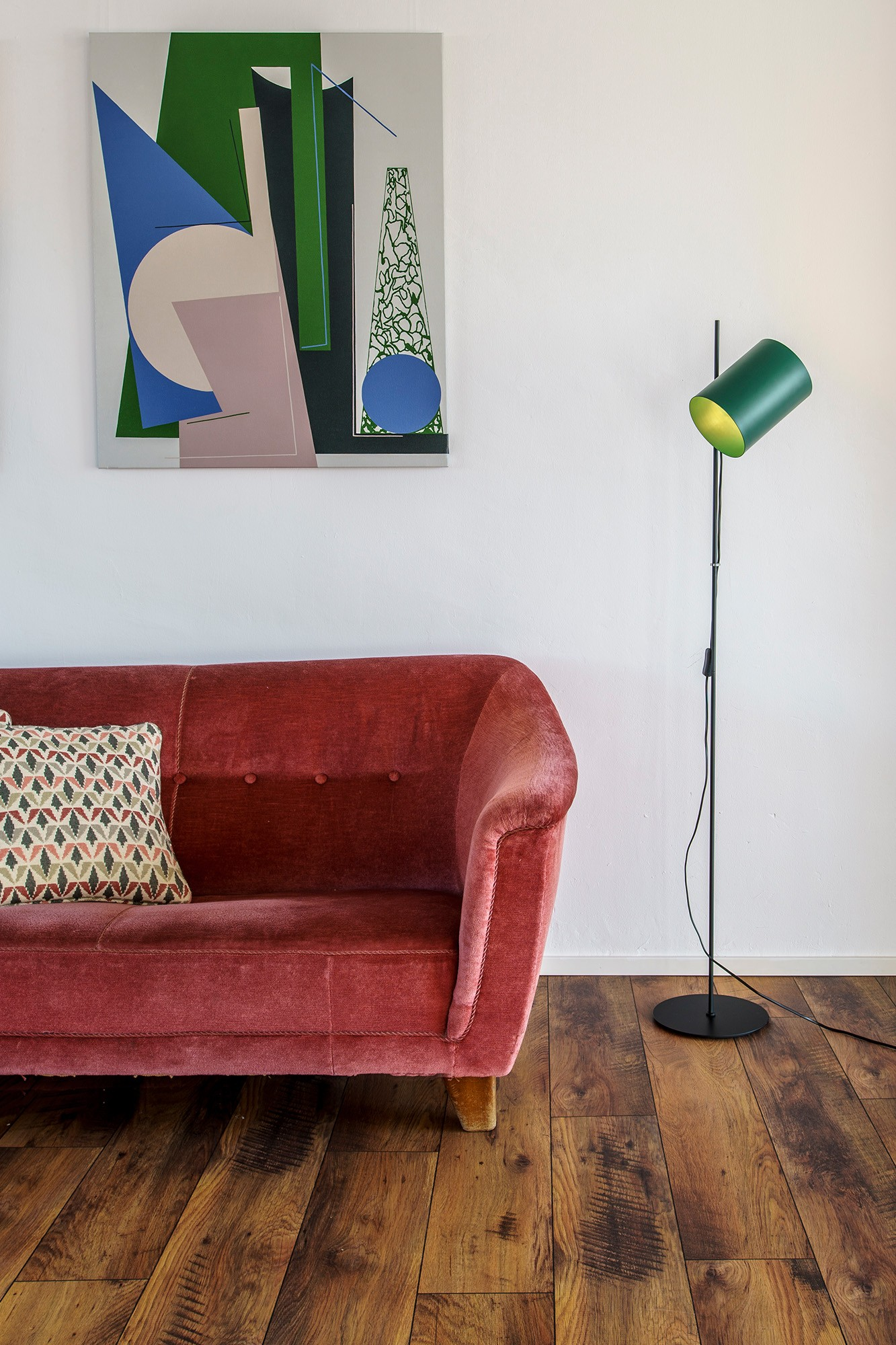 Un soggiorno con divano rosso, arte astratta, pavimento in legno e lampada verde.