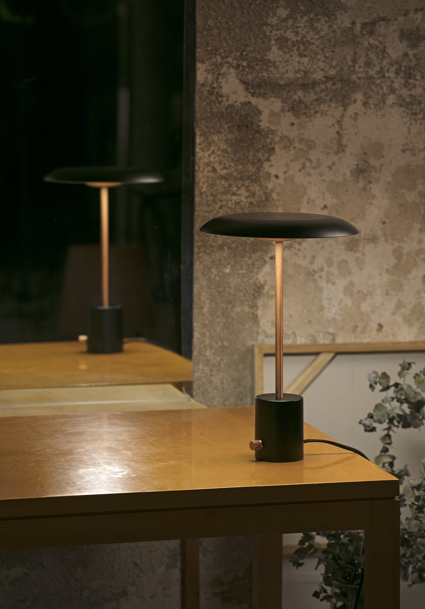 Lampada da tavolo nera con base nera e stelo in rame, riflessa in uno specchio.