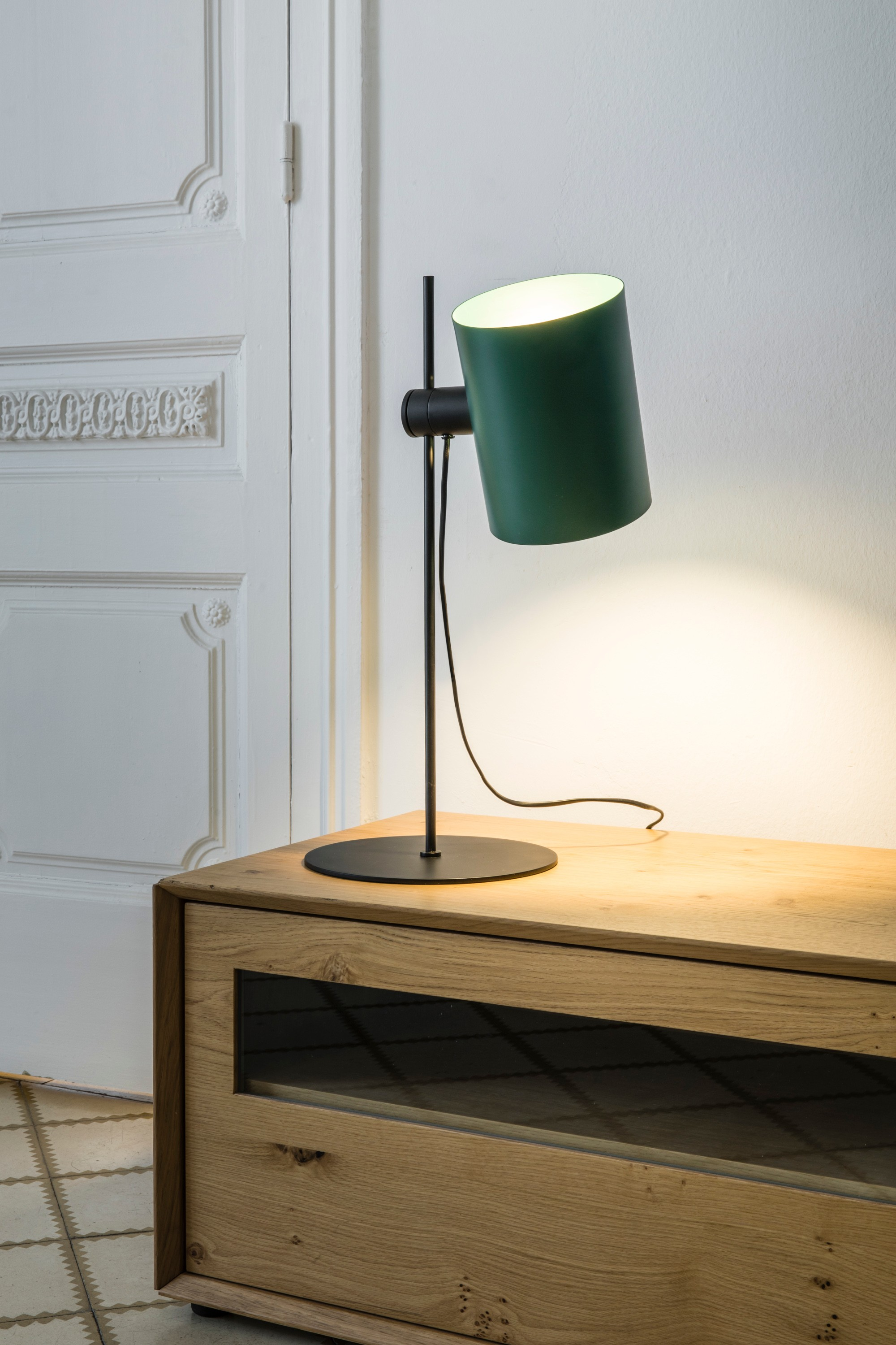 Lampada verde su tavolo di legno. Muro bianco e porta di legno sullo sfondo.