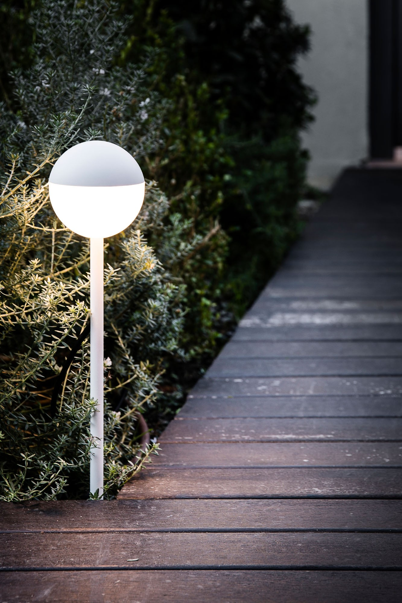 Un lampione esterno illuminato accanto a una passerella di legno.