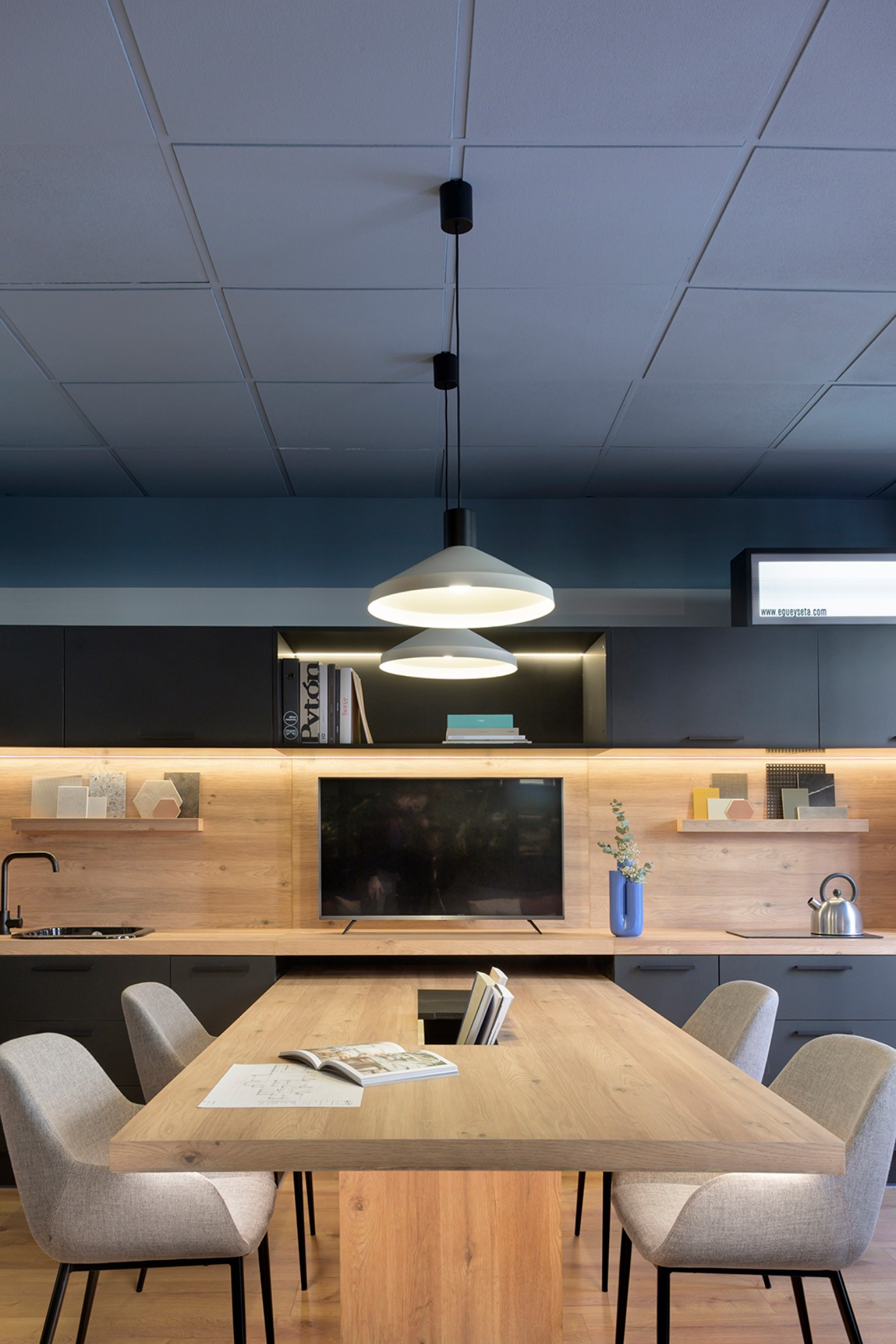 Cucina moderna con mobili in legno, luci, tavolo, sedie, TV e decorazioni.