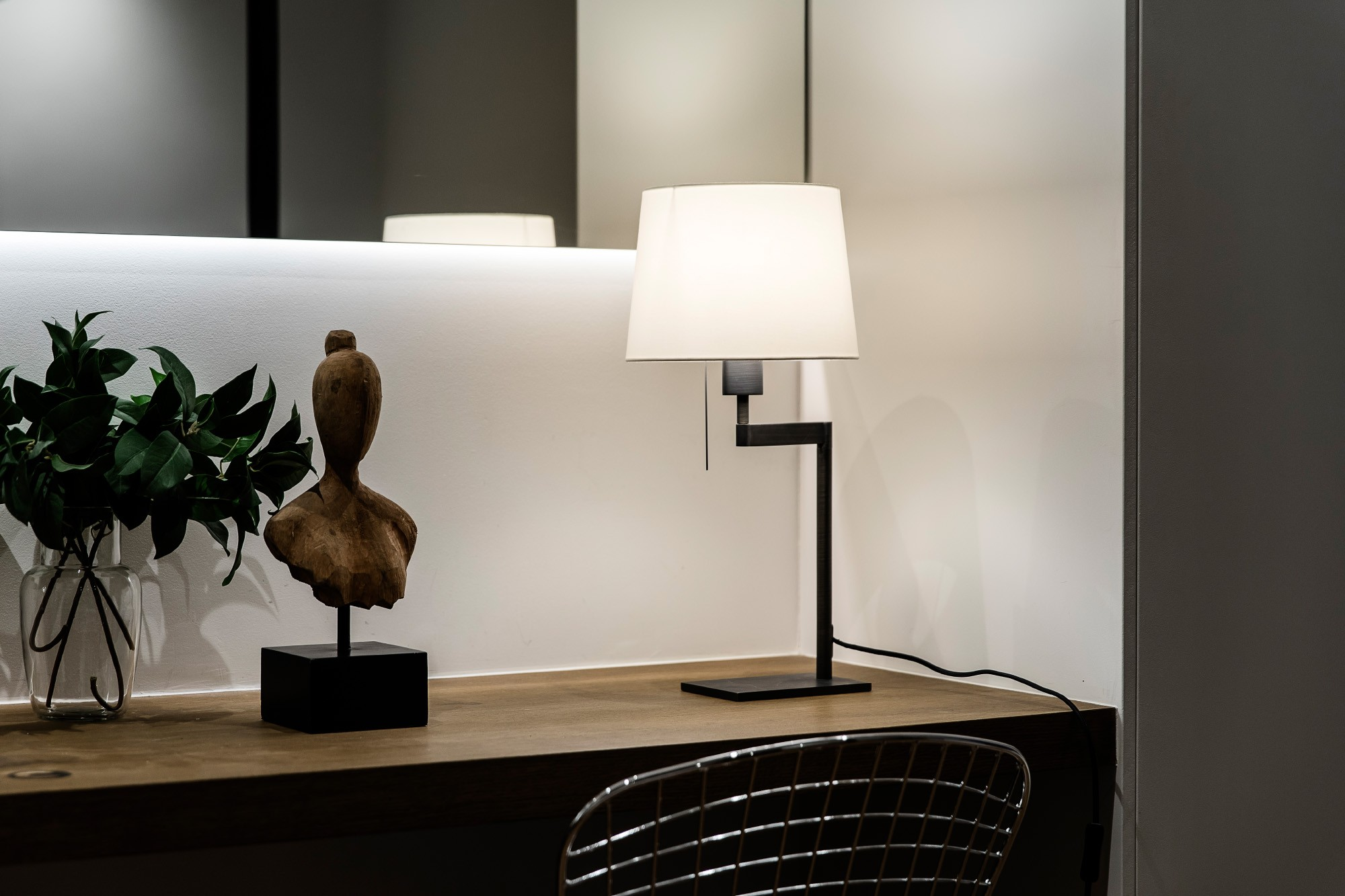 Ein Schreibtisch mit Lampe, Skulptur und Vase mit grünen Blättern.