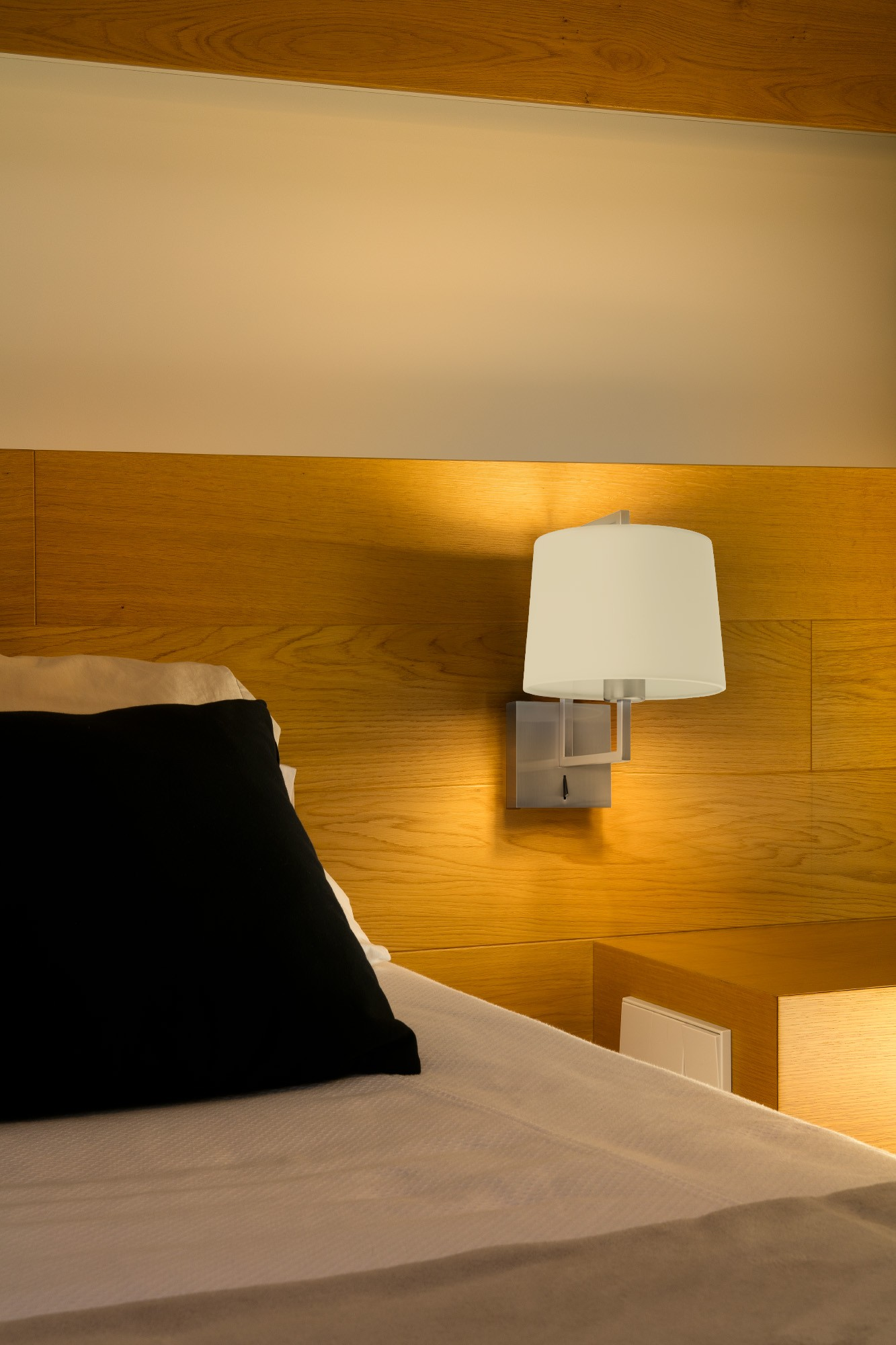 Camera da letto con lampada a parete, letto e cuscino nero.