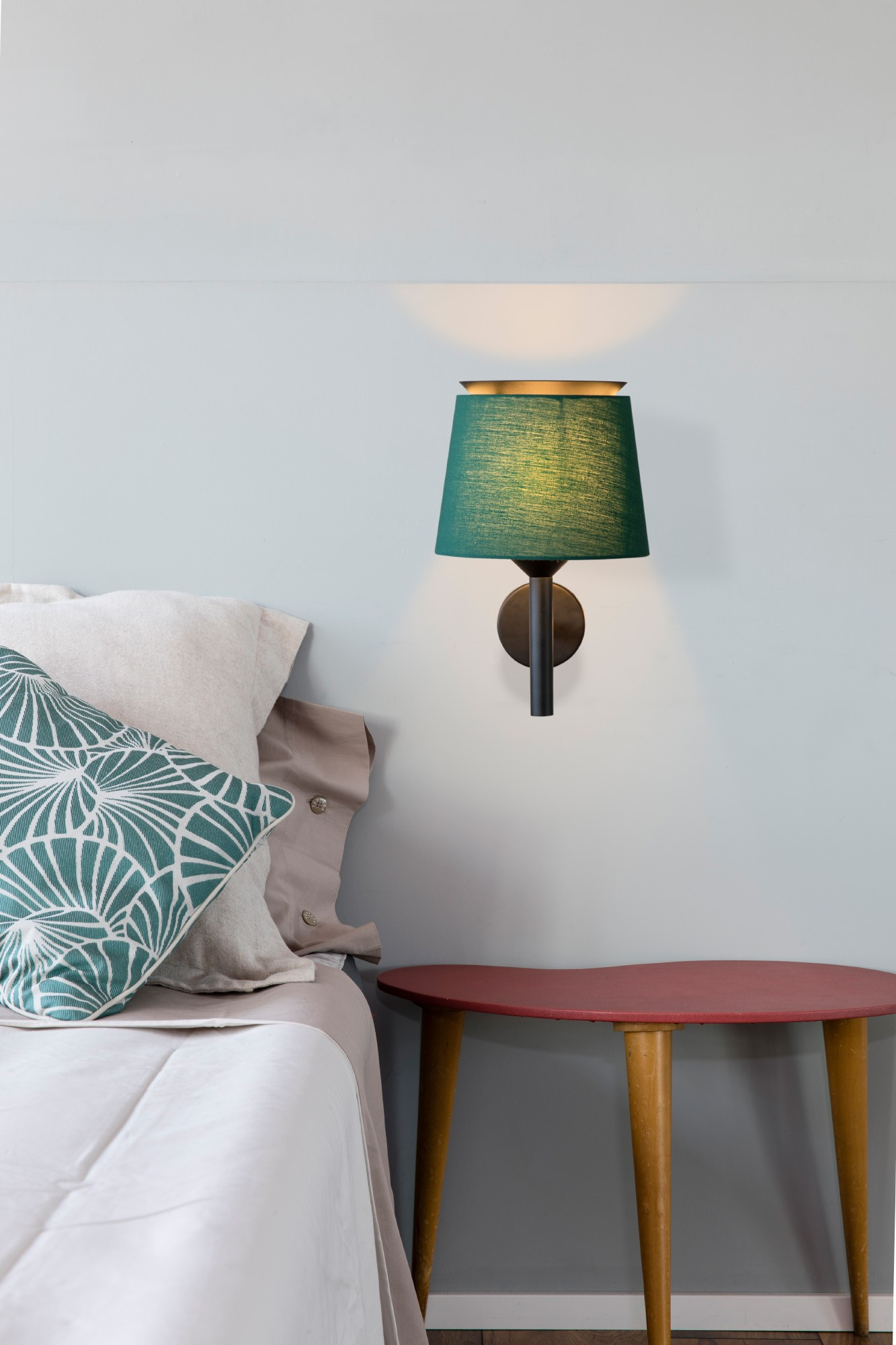 Camera da letto con paralume verde acqua. Letto con cuscini e comodino rosso.