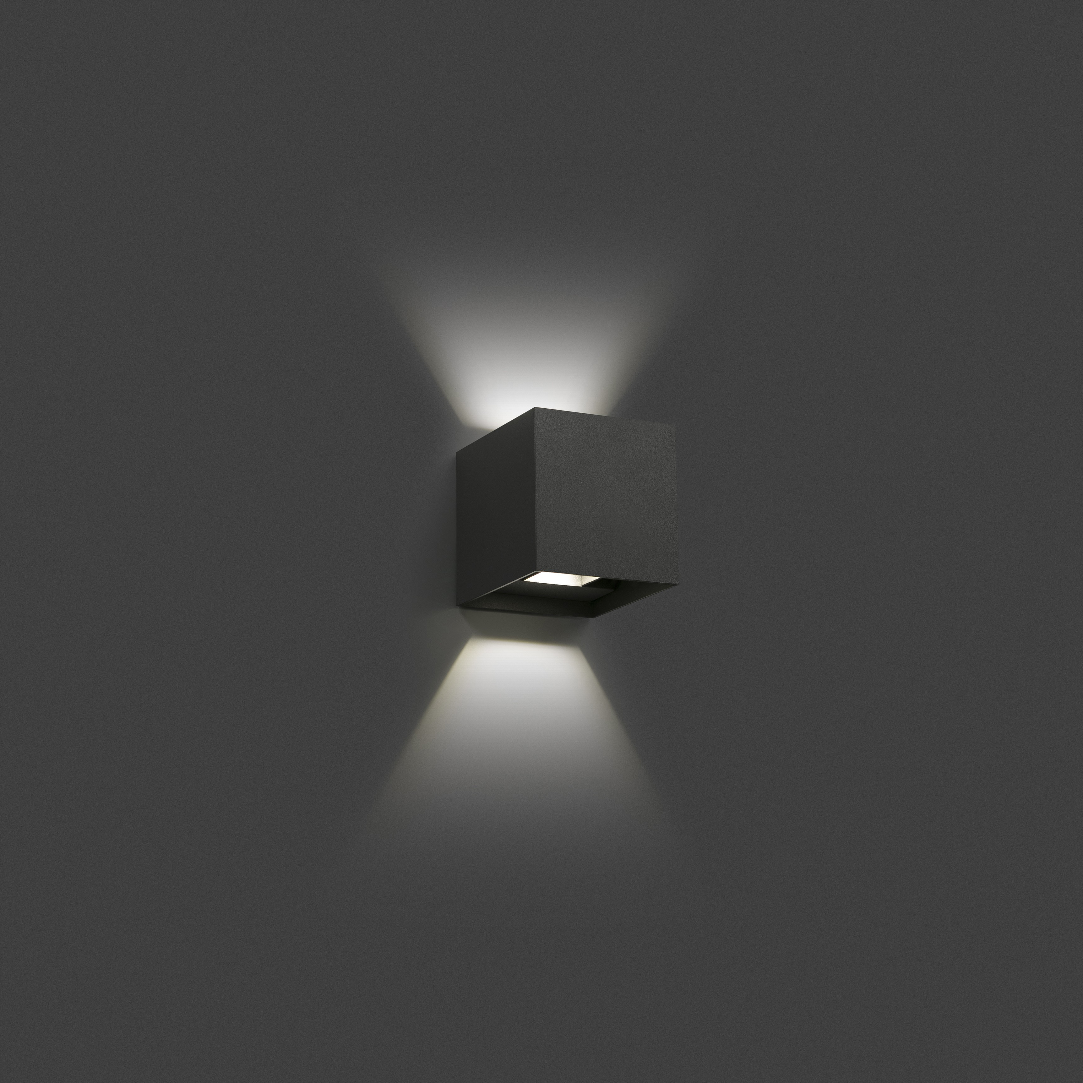 Una lampada da parete quadrata nera. Emette luce verso l'alto e verso il basso. Lo sfondo è una parete grigio scuro.