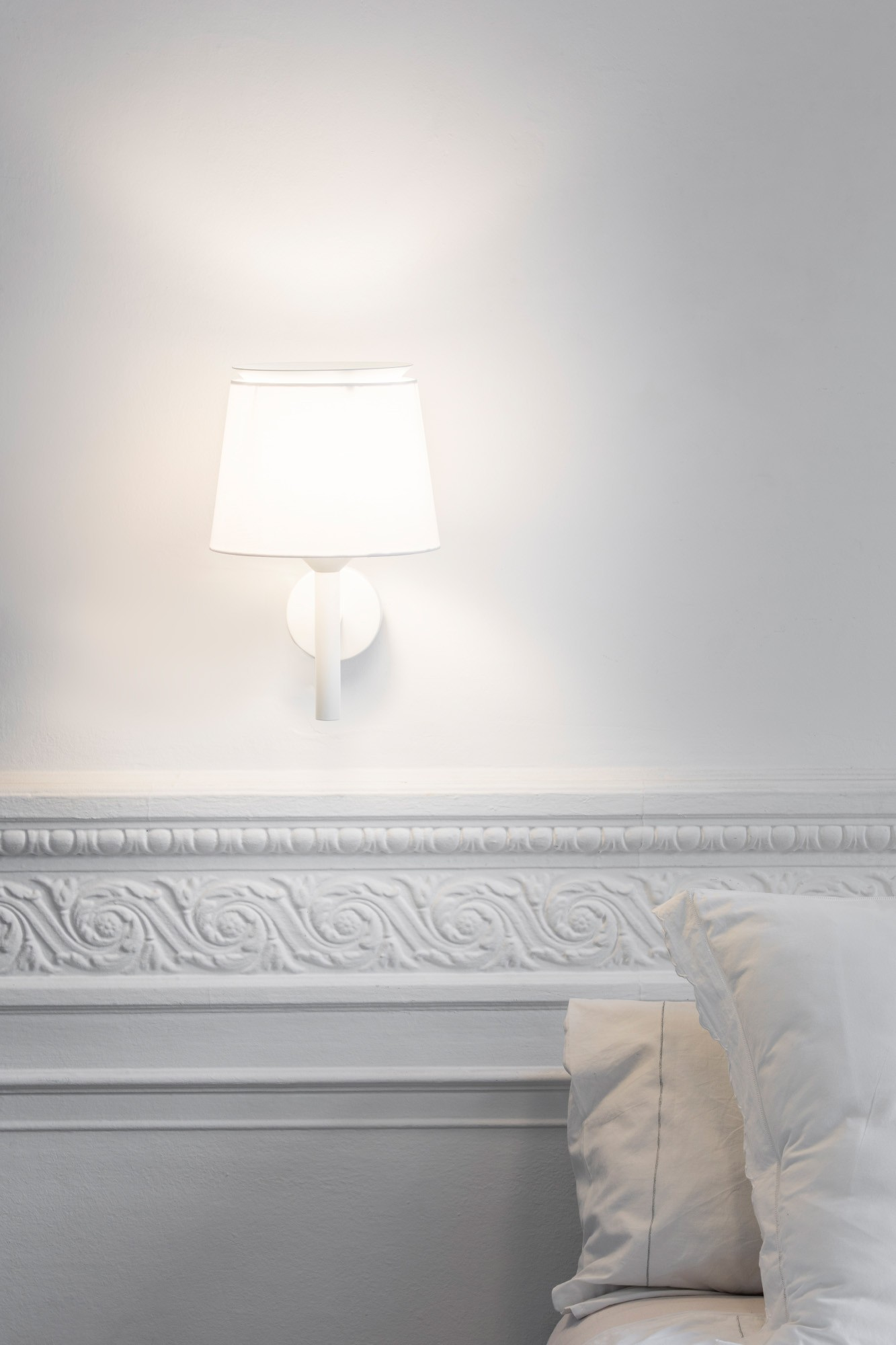 Parete bianca con una lampada bianca e una modanatura bianca decorativa sottostante.