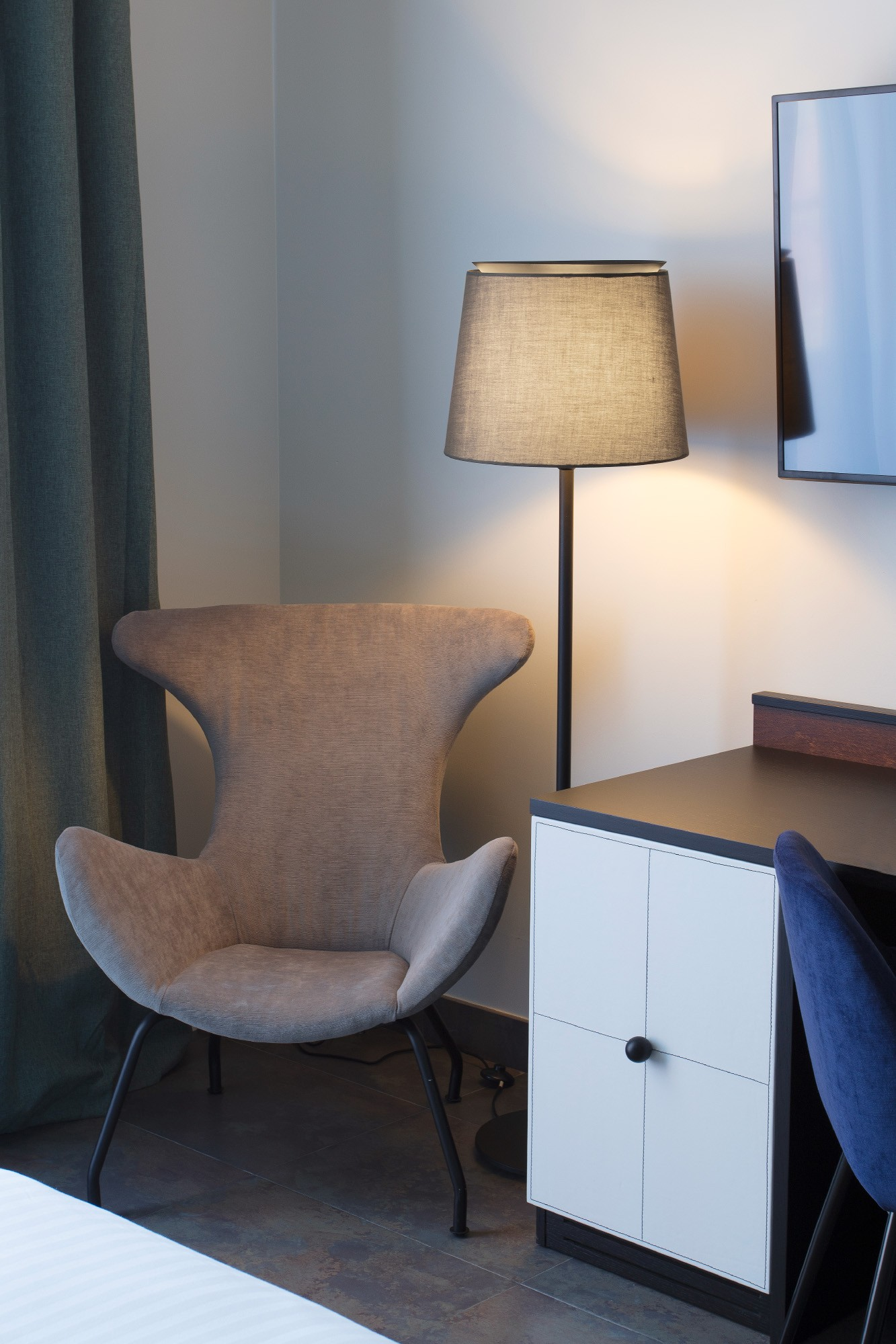 Un angolo della stanza con una lampada da terra, una sedia grigia, un armadio e una TV.