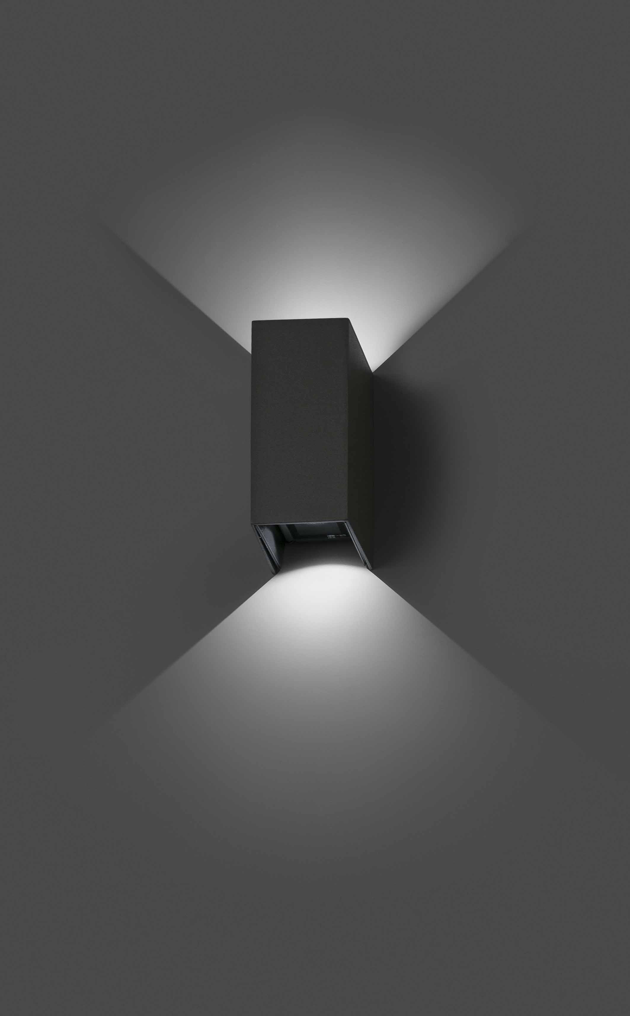 Lampada da parete con corpo rettangolare grigio scuro. Proietta luce verso l'alto e verso il basso.