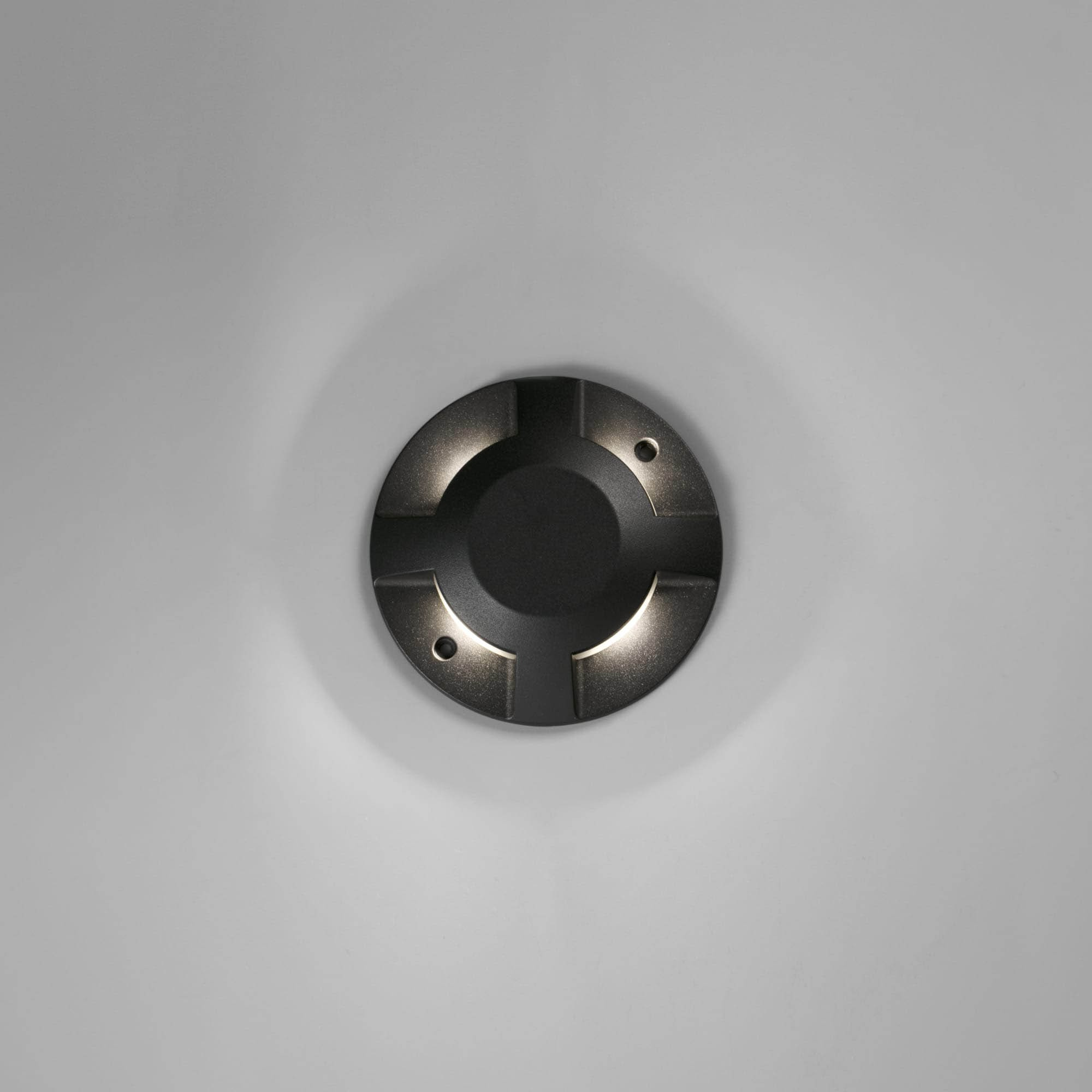 Lampada rotonda nera per esterni su un muro bianco. La lampada ha quattro fasci di luce.
