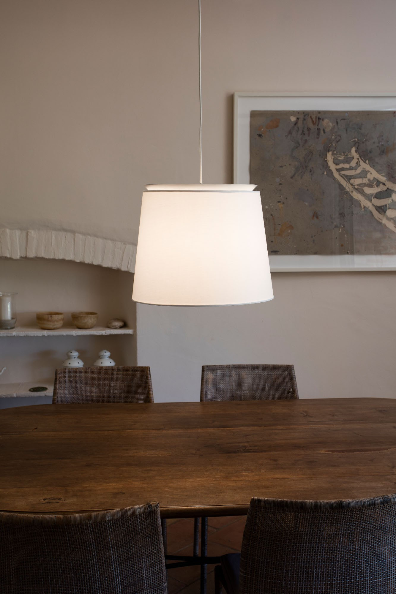 Lampada a sospensione sopra un tavolo di legno. Due sedie sotto. Arte sulla parete sullo sfondo.
