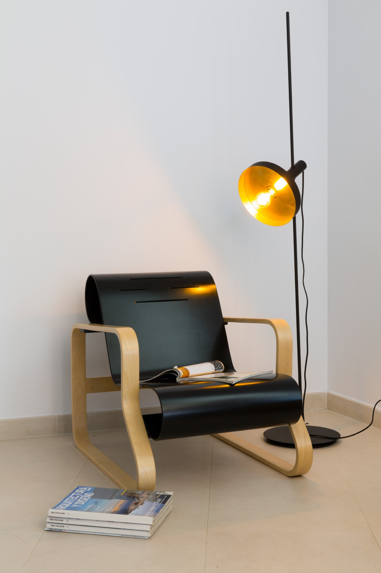 Lampada da terra con sedia e riviste. Libri sul pavimento a sinistra.