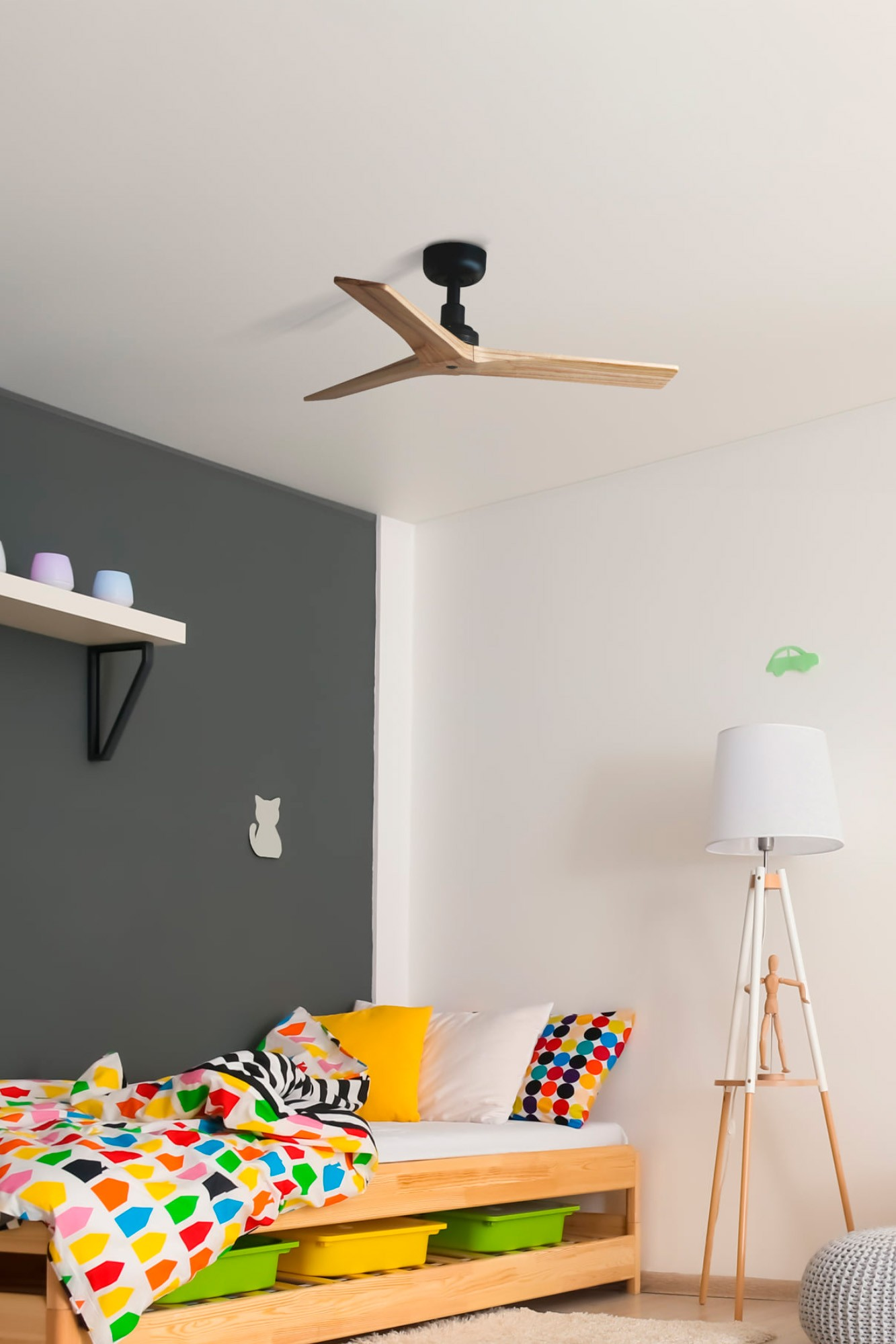Camera da letto con letto in legno e ventilatore a soffitto. Copriletto colorato, cuscini gialli e bianchi.