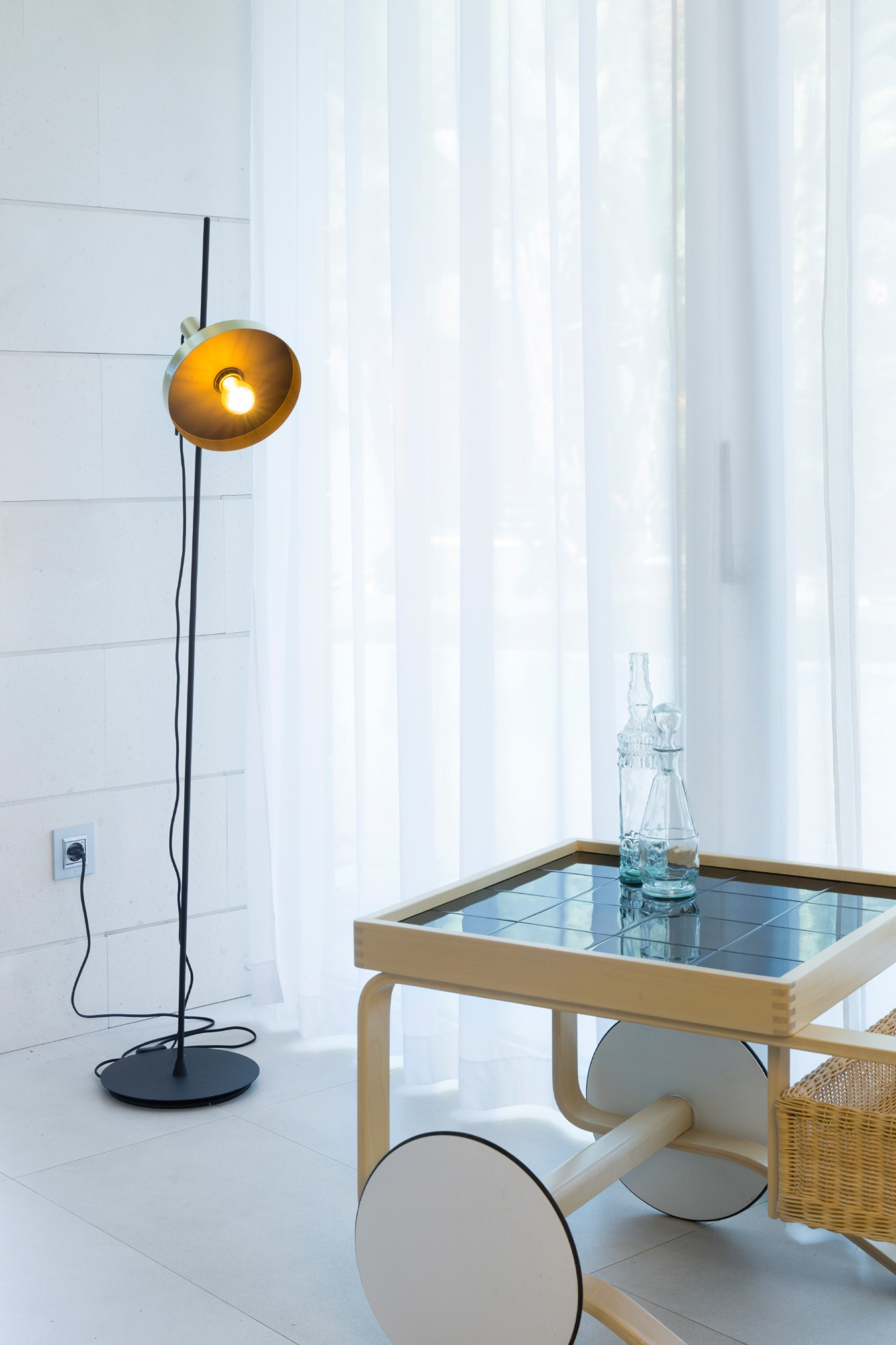 Lampada da terra con tavolo in vetro e sedia. Tende sul lato destro.