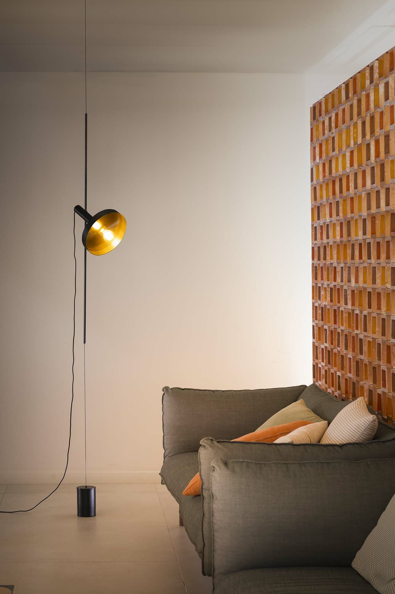 Una lampada da terra con un faretto, un divano e un muro di mattoni sullo sfondo.