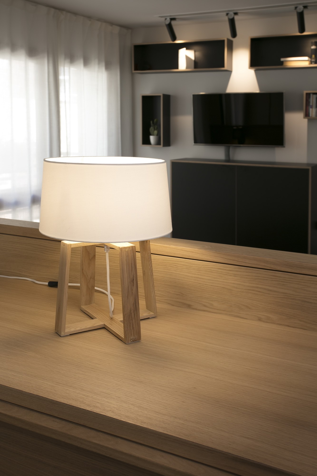 Weiße Lampe mit Holzfuß auf einem Holztisch in modernem Raum.