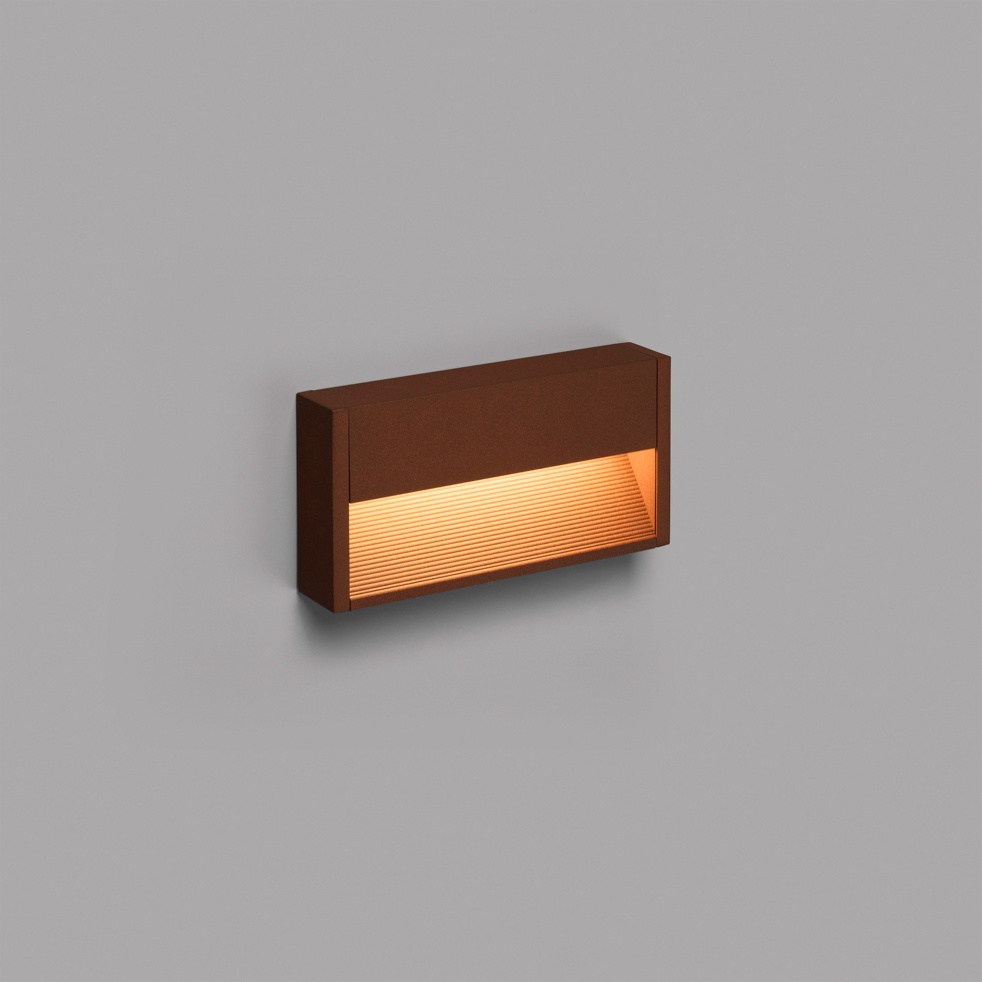 Applique da parete rettangolare marrone su un muro grigio. La luce brilla dall'interno.