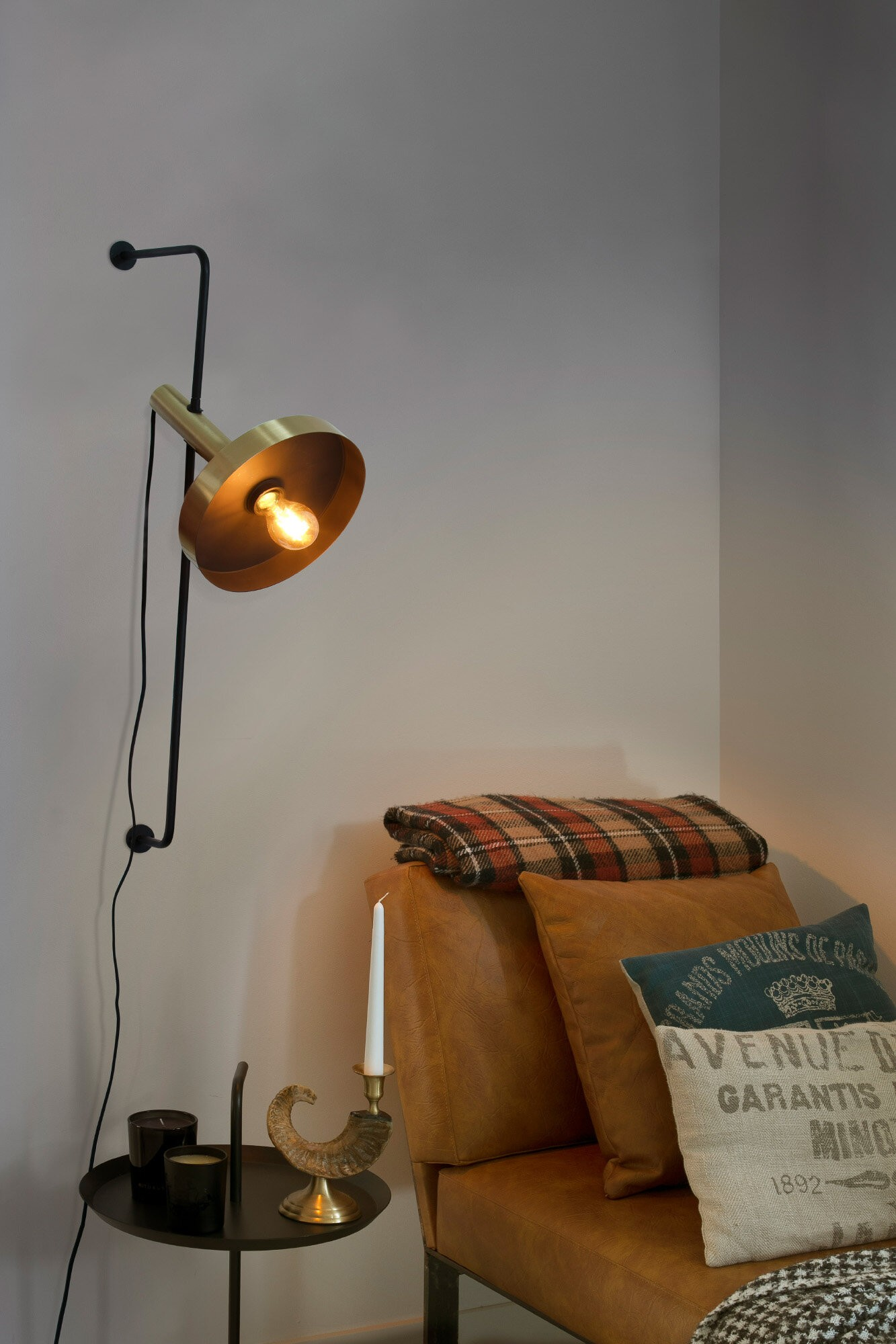 Una lampada da parete con paralume dorato, vicino a un divano in pelle marrone.