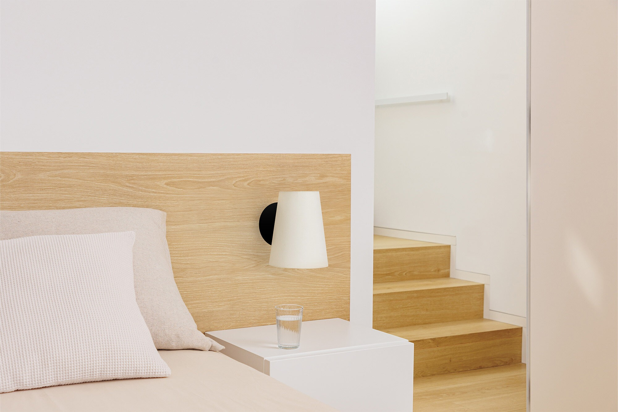 Scena del comodino con lampada, libro e bicchiere d'acqua su comodino bianco.