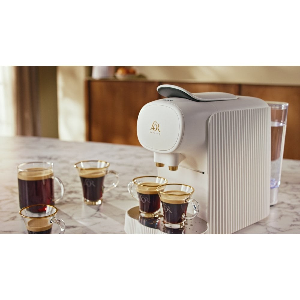 Macchina da caffè bianca con tre tazze di caffè e un bicchiere d'acqua.