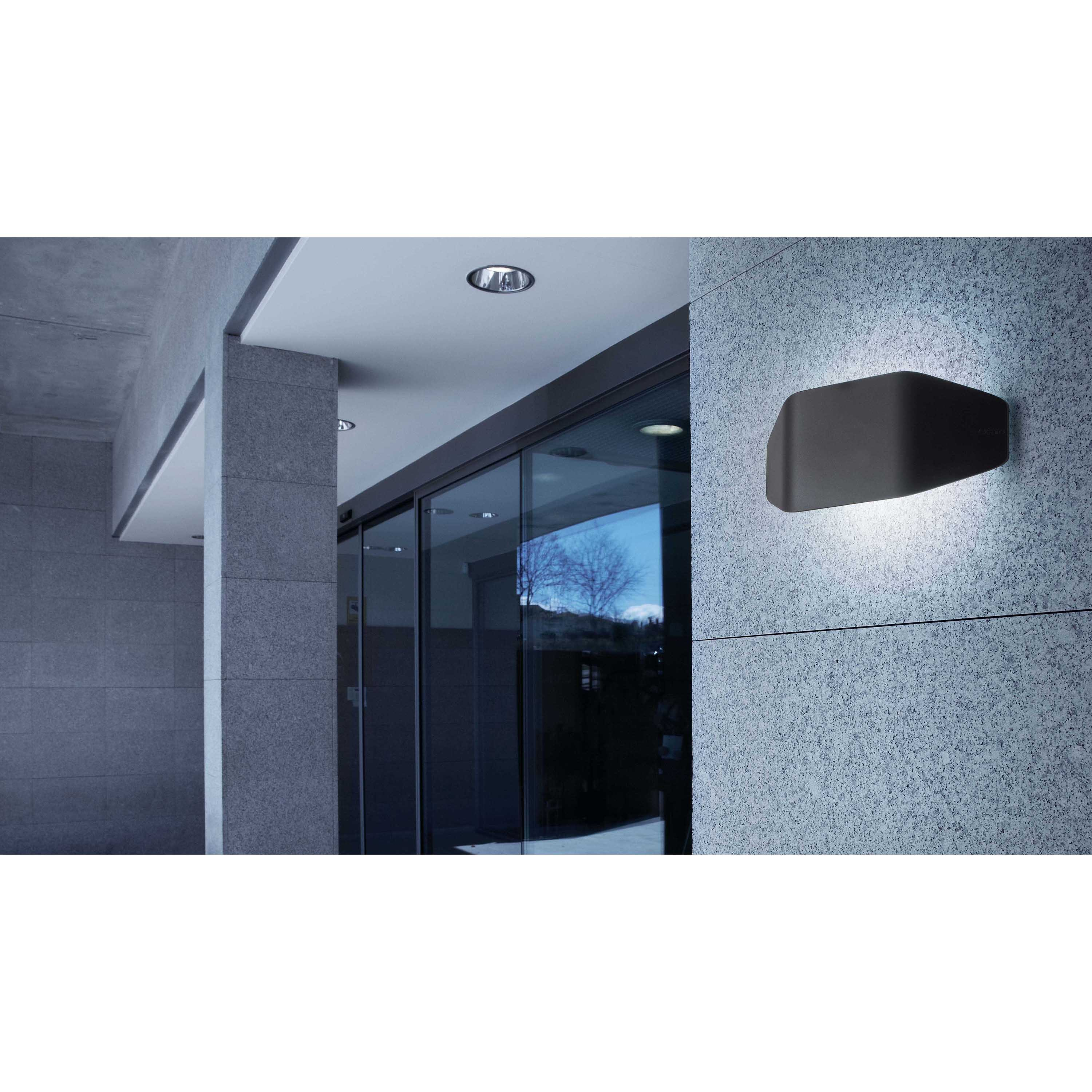Un'applique a parete su un muro strutturato, vicino a una porta a vetri e a colonne di pietra. La luce è accesa.