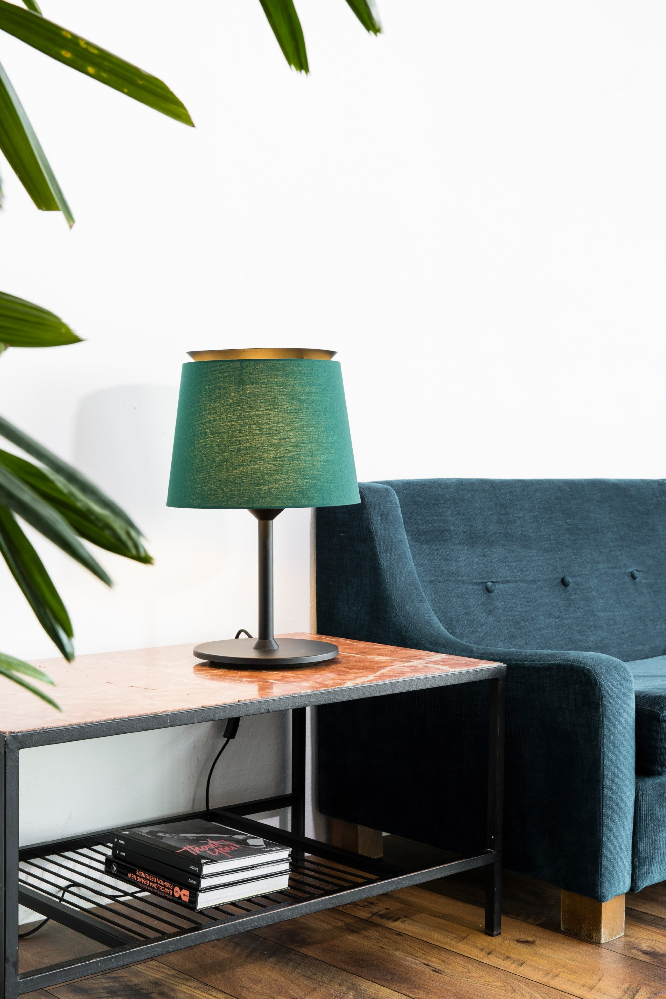 Lampada verde con paralume scuro su un tavolo, con un divano blu sullo sfondo.