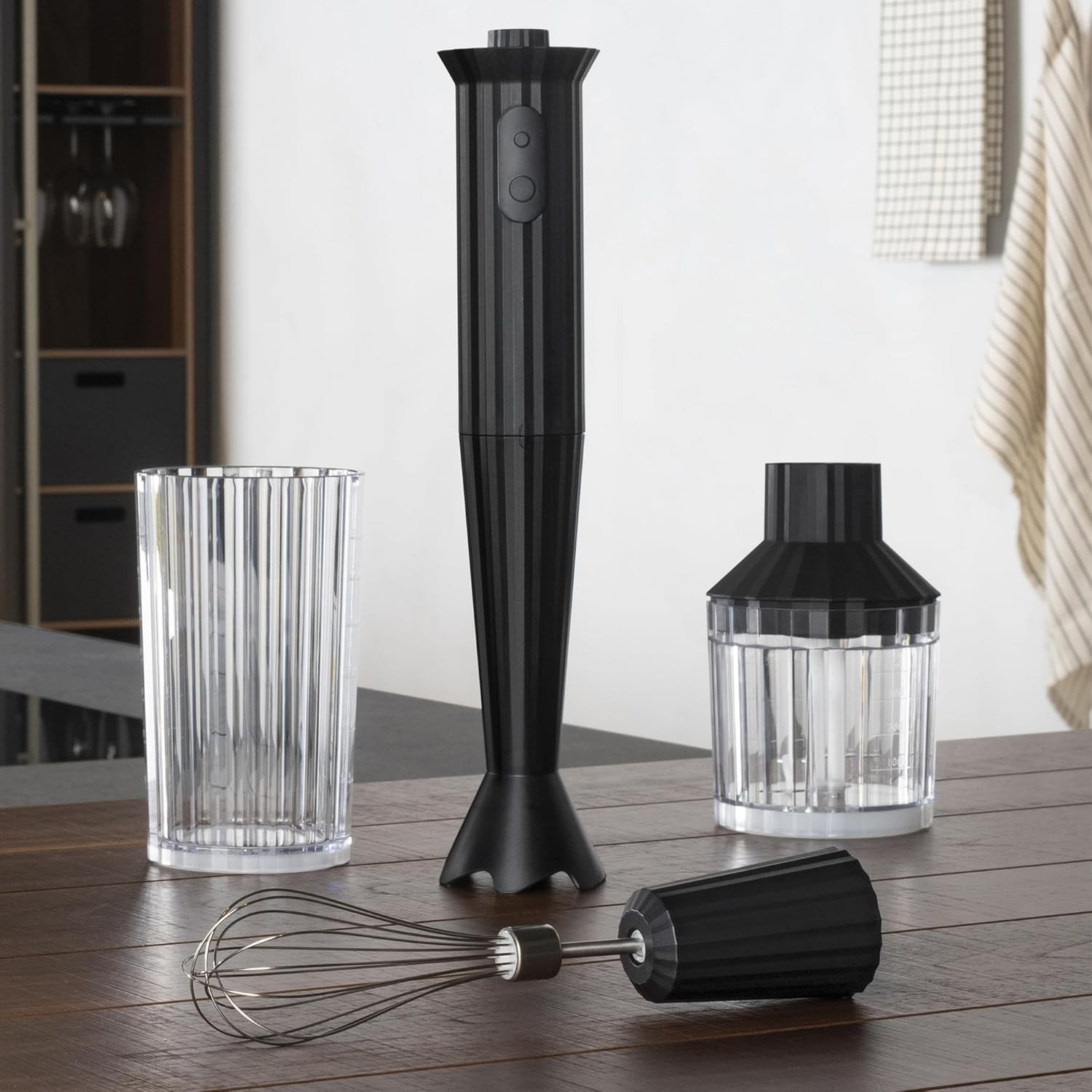 Set frullatore a immersione nero con accessori su un tavolo di legno, ambiente cucina.