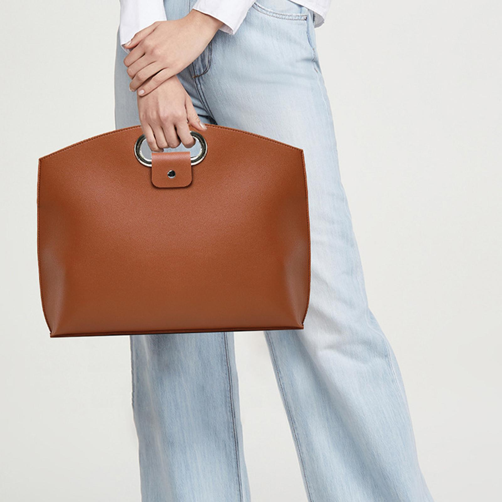 Person hält eine braune Handtasche und trägt blaue Jeans.