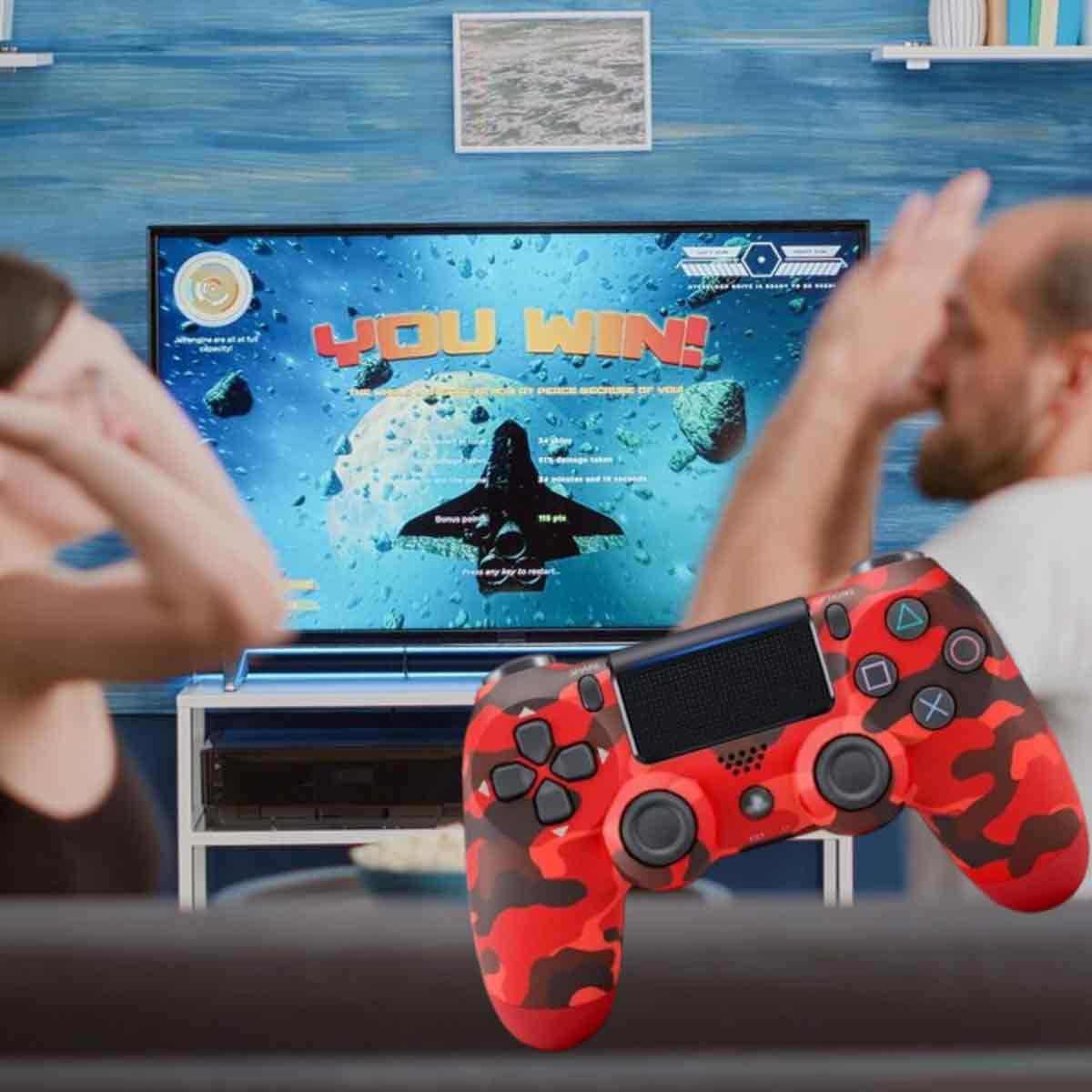Mann hält einen roten Camouflage-Controller, im Hintergrund ein Fernseher mit Spielbildschirm.