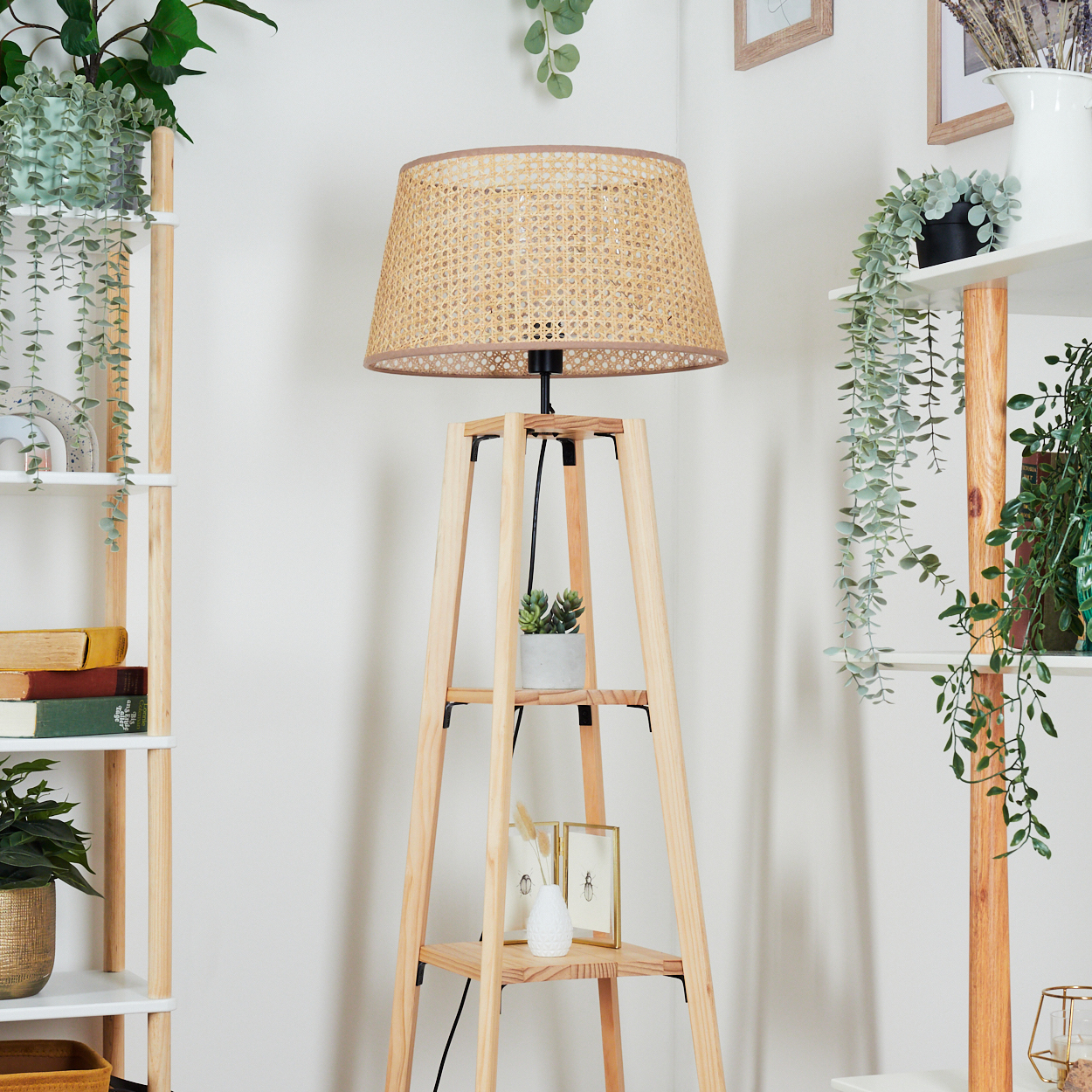 Holzlampe mit gewebtem Schirm, Regale mit Pflanzen und Dekoration, Hängepflanzen, alles vor einer weißen Wand.