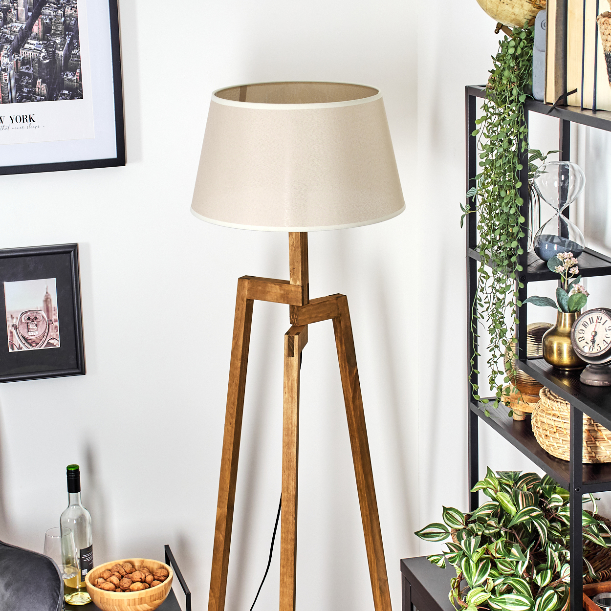 Stehlampe aus Holz mit beigem Lampenschirm, in der Nähe eines Regals mit Deko.