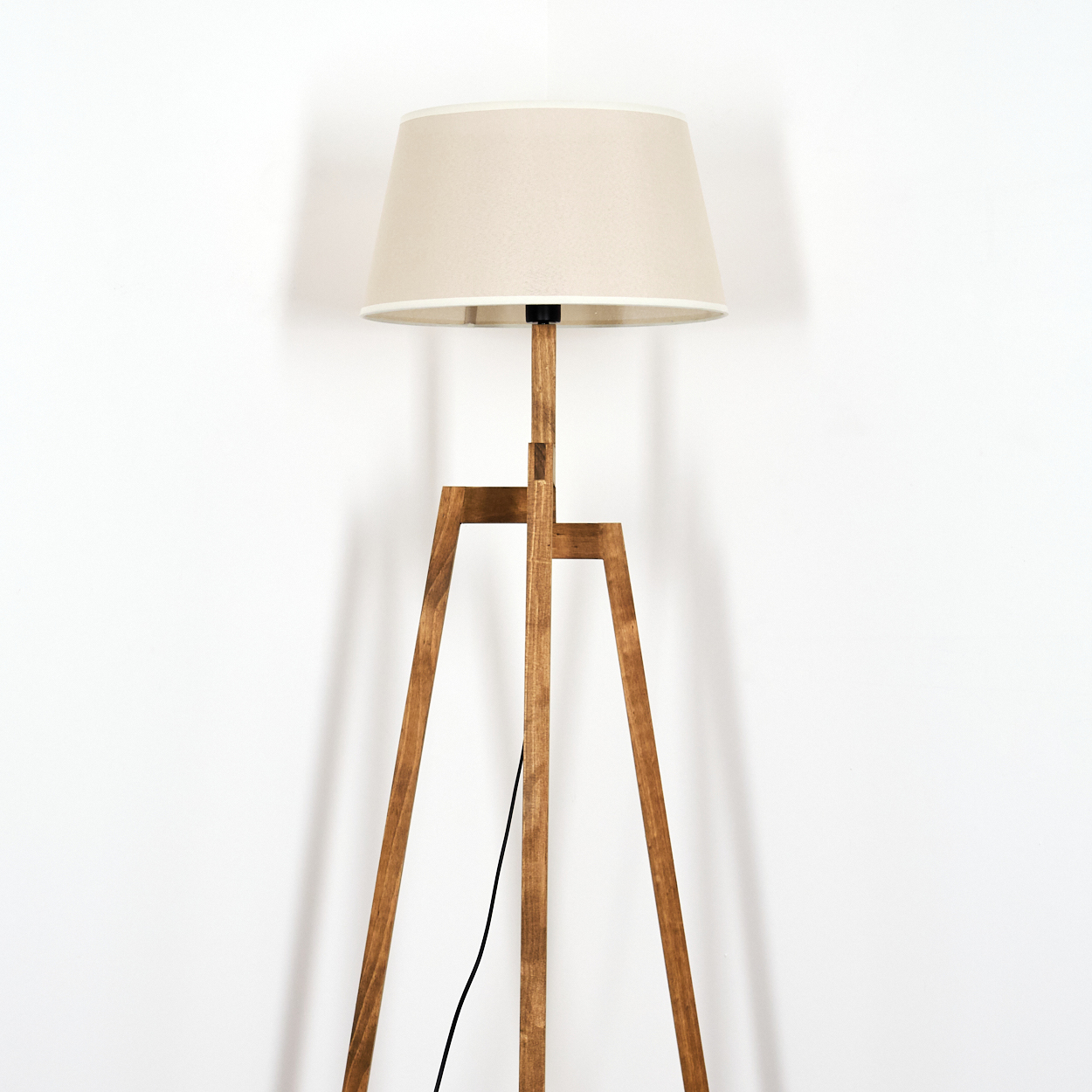 Holz-Stehlampe mit beigem Lampenschirm. Schwarzes Kabel. Weißer Hintergrund.