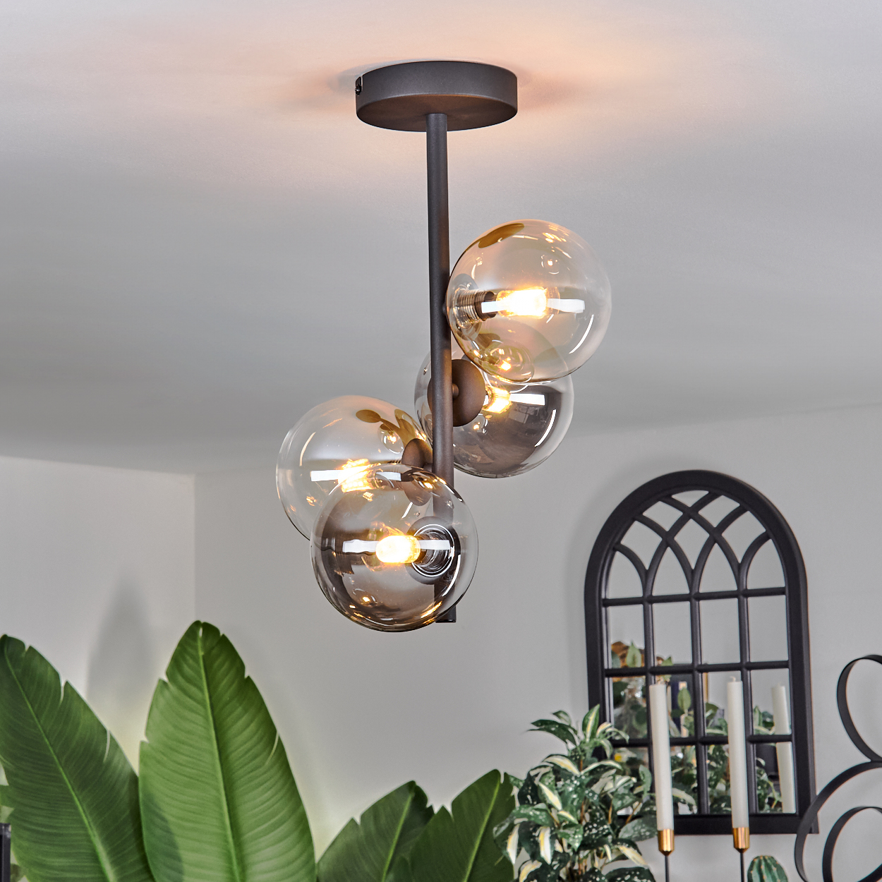 Eine Deckenlampe mit vier beleuchteten Glaskugeln in einem Raum mit Pflanzen und einem dekorativen Bogen.