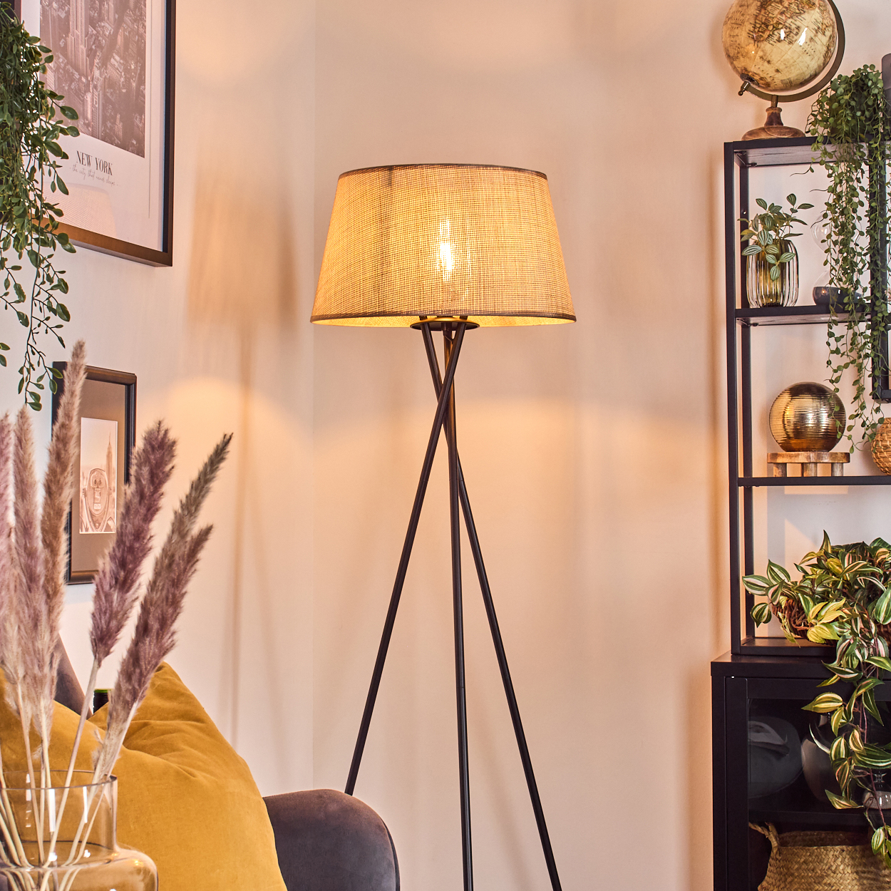 Ein Zimmer mit beleuchteter Stehlampe, schwarzem Dreibein-Fuß und beigem Schirm, schafft warme Atmosphäre.