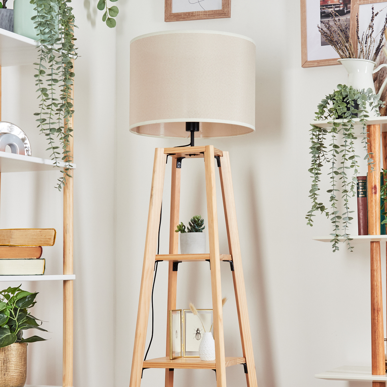 Eine hölzerne Stehlampe mit zwei Regalen, cremefarbenem Lampenschirm und Dekoration, neben Regalen.