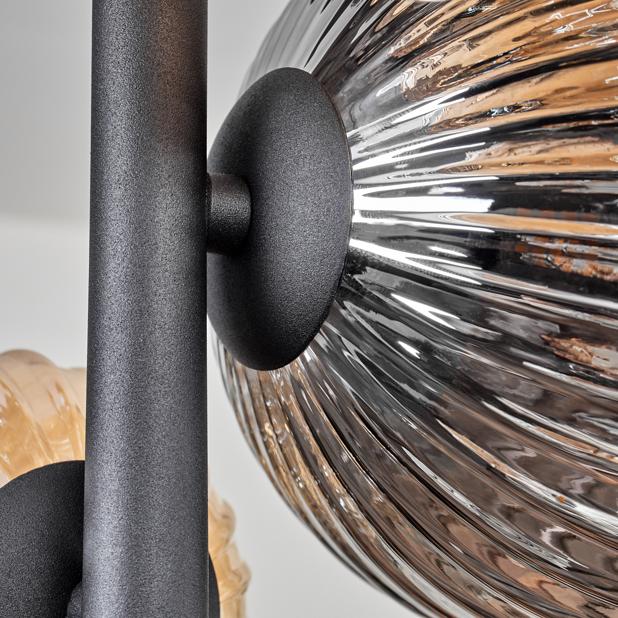 Nahaufnahme einer schwarzen Metalllampenstruktur mit silbernen und bernsteinfarbenen Kugeln. Weißer Hintergrund.