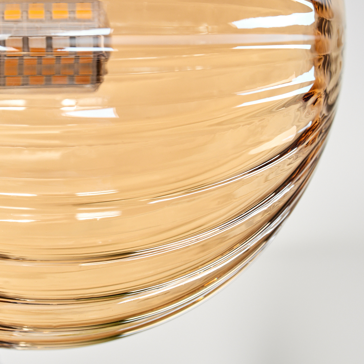 Nahaufnahme einer gerippten bernsteinfarbenen Glaskugel mit einer LED-Leuchte. Weißer Hintergrund.
