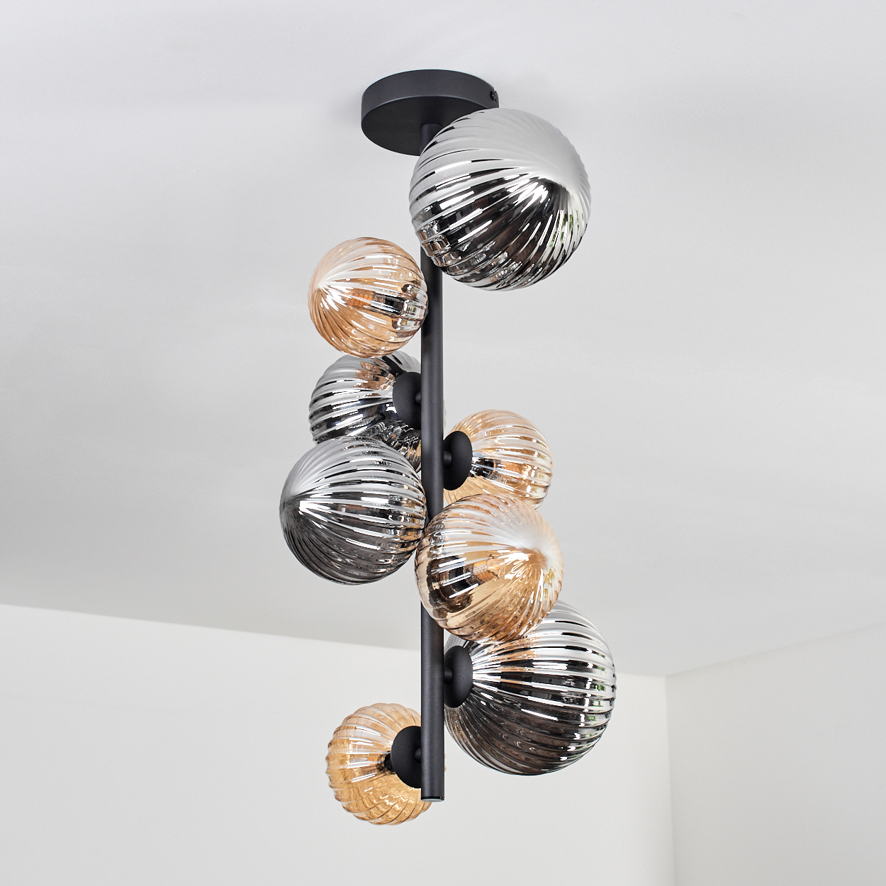 Eine Lampe mit silbernen und bernsteinfarbenen Glaskugeln, die von der Decke hängt. Weißer Hintergrund.