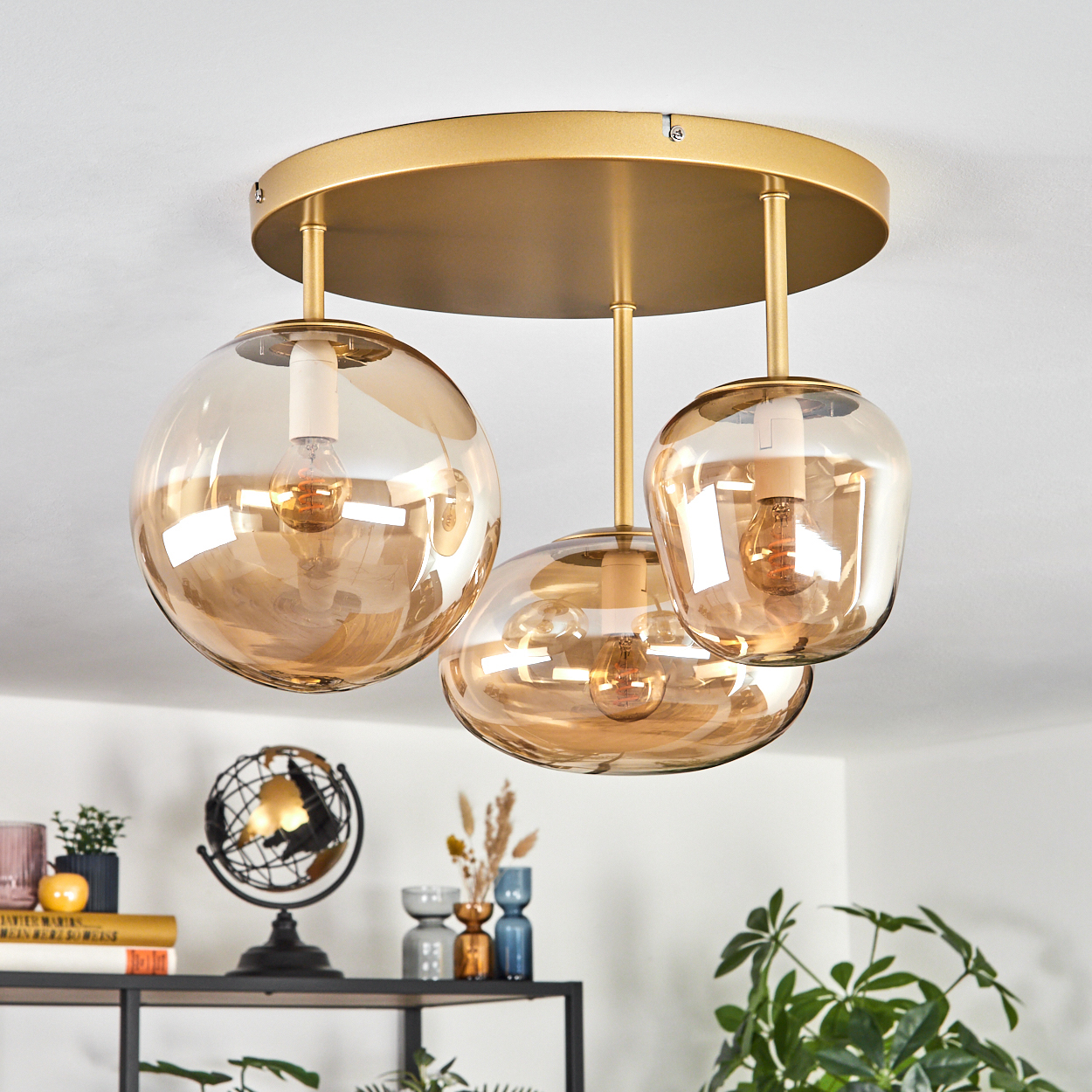 Drei bernsteinfarbene Glaskugel-Hängeleuchten hängen von der Decke, mit einer goldenen Platte.