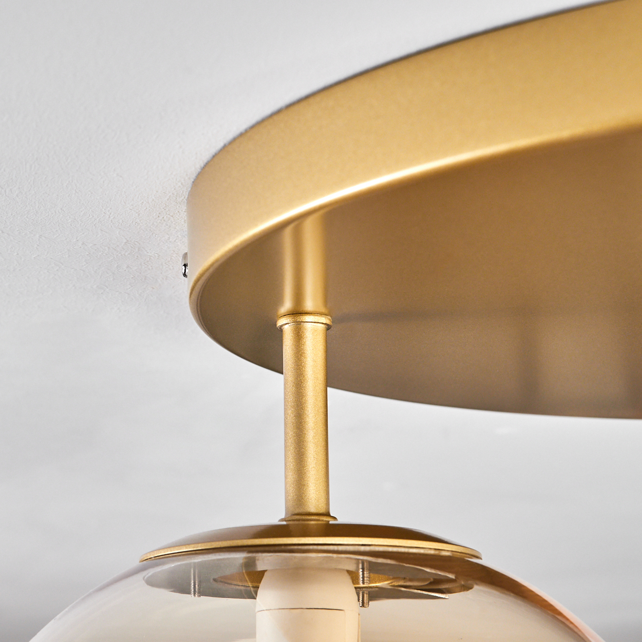 Nahaufnahme einer goldenen Deckenplatte mit einer goldenen Stange und einer bernsteinfarbenen Glaskugel.