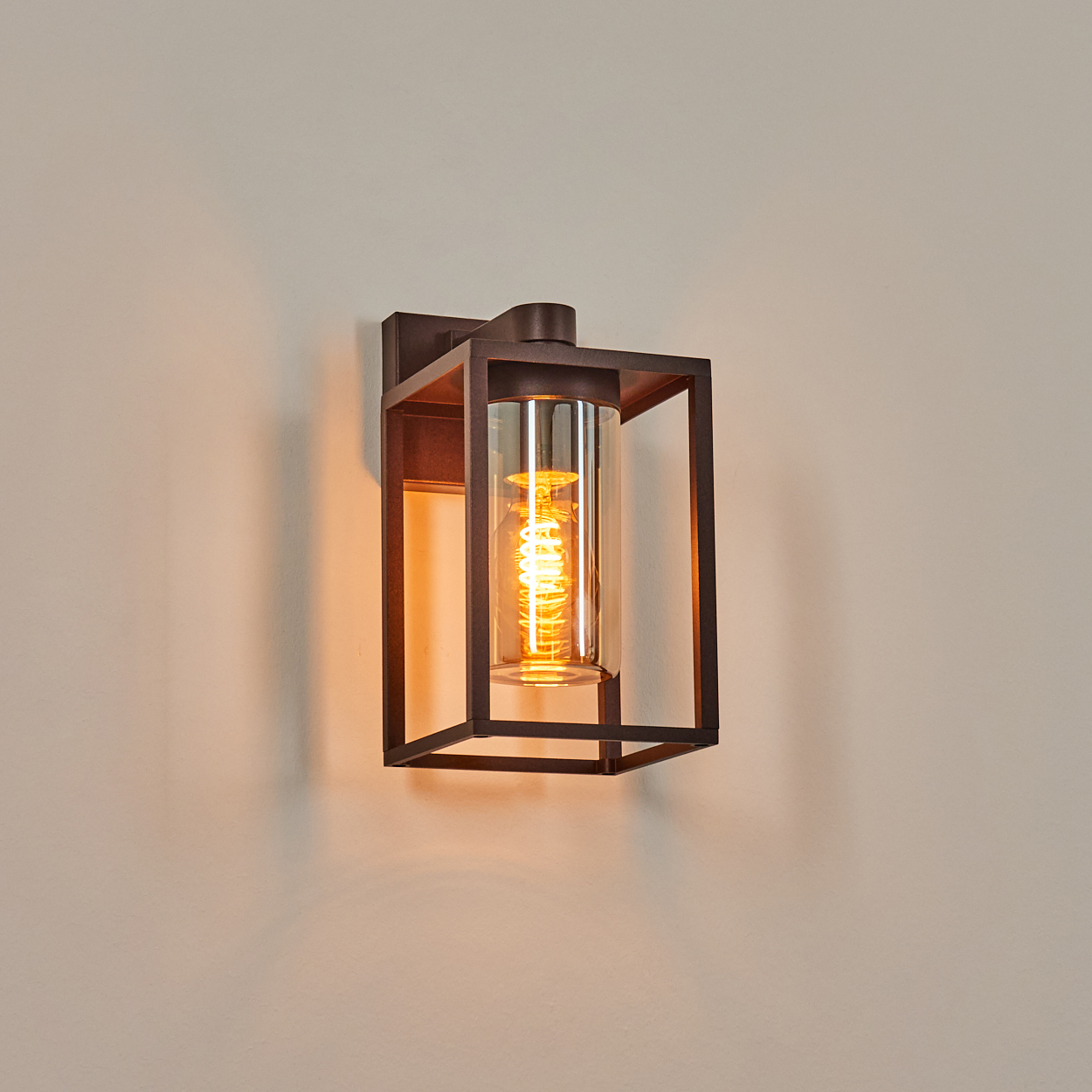 Eine bronzefarbene Wandleuchte mit Glasröhrenschirm leuchtet an der Wand.
