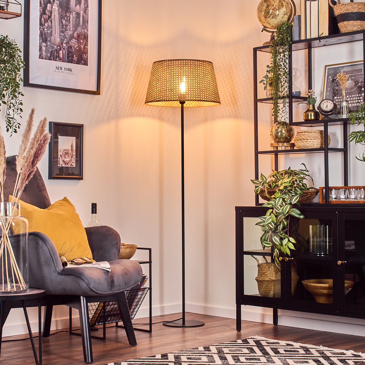 Stehlampe im Wohnzimmer. Gewebter Lampenschirm, schwarzes Gestell. Inneneinrichtung mit Pflanzen.