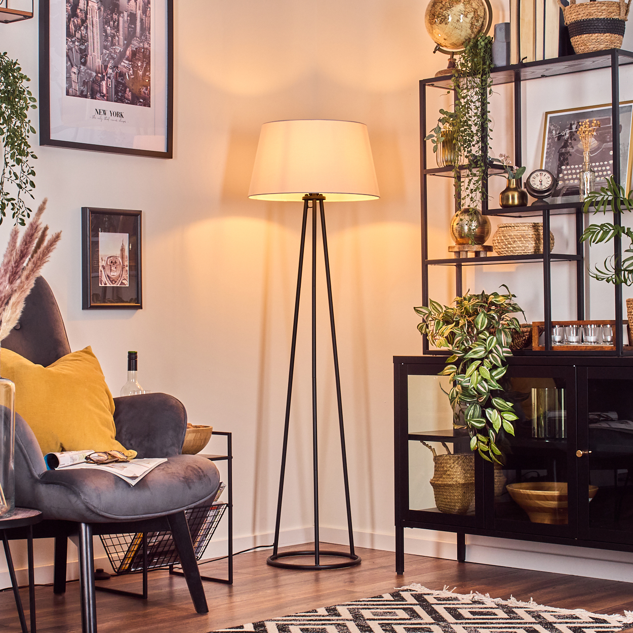Wohnzimmer mit Stehlampe, Sessel und schwarzem Schrank. Pflanzen und Dekor ergänzen die Szene.